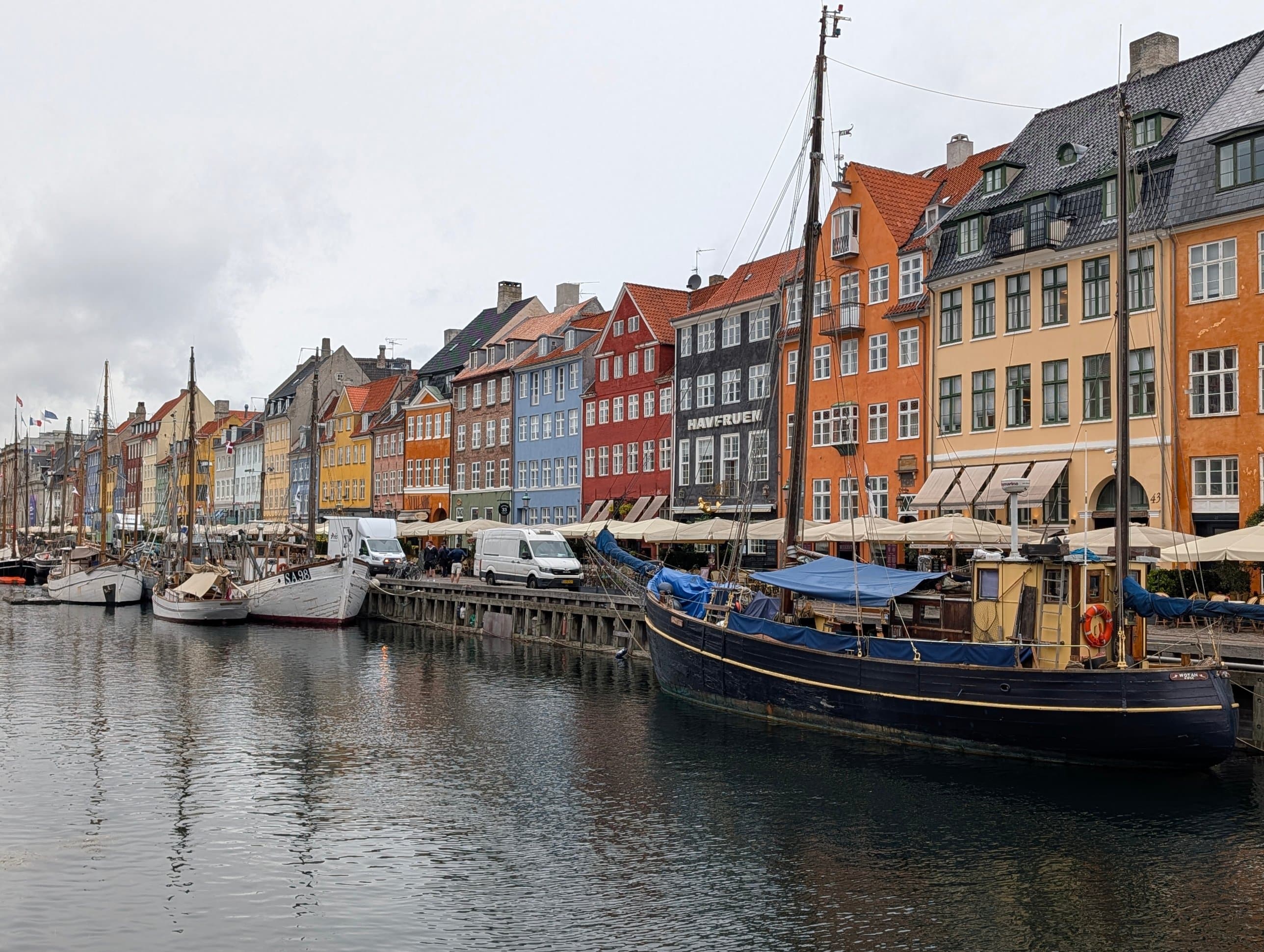 Colourful merchant houses in red, orange, blue and yellow along the Nyhavn canal in Copenhagen, with wooden sailing boats moored in the foreground