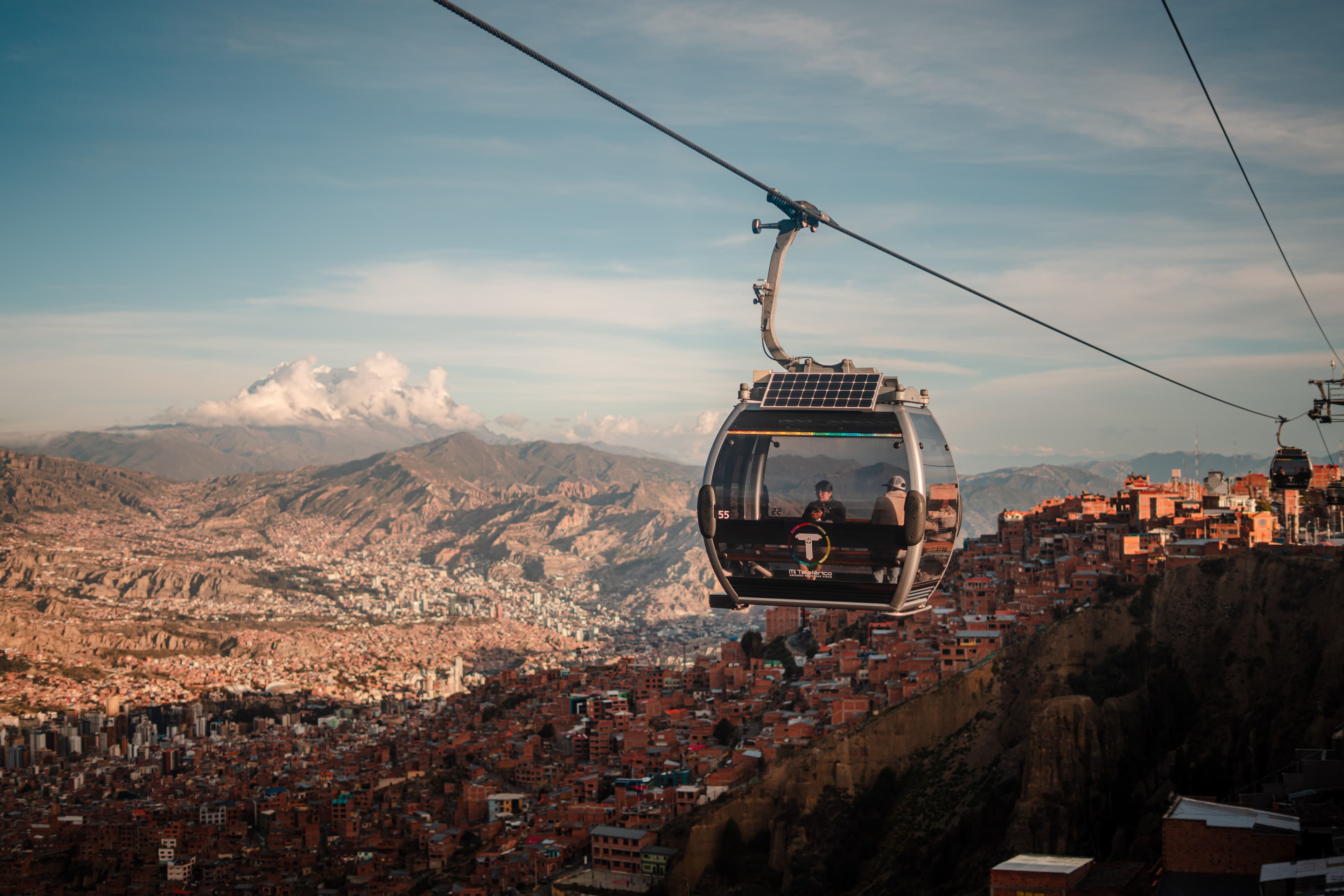 A red Mi Teleférico cable-car gondola high above the rooftops of La Paz, with the city climbing the hillside beneath a bright sky