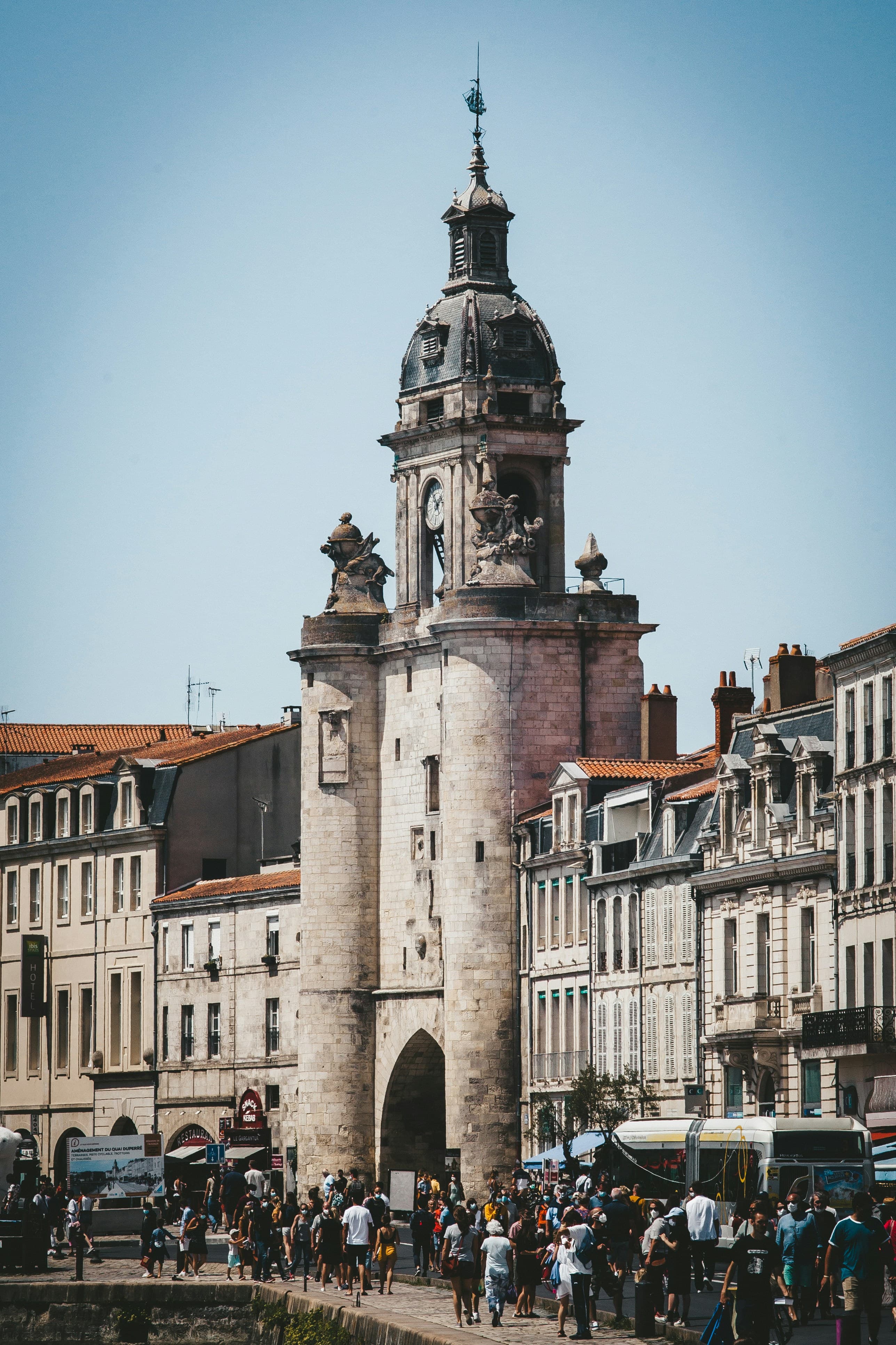 The Grosse Horloge, La Rochelle's medieval clock-tower gate, rising above the crowds on the quayside with its domed belfry and carved stonework against a clear sky.