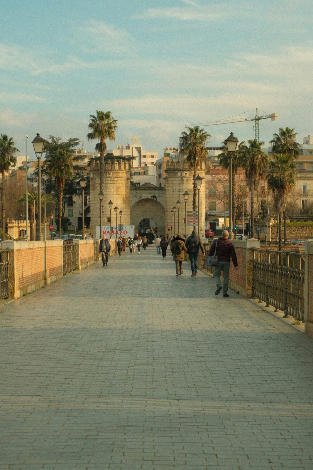 Walkers on the paved deck of Puente de Palmas leading to the two round towers of Puerta de Palmas, the river gate the Maratón de Badajoz passes five times, at km 16.5, 24.6, 31.7, 33.1 and 36.6