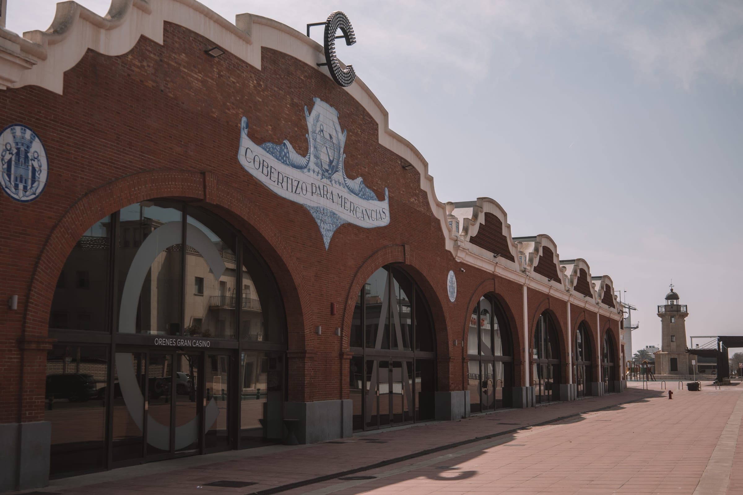 A red-brick arcaded warehouse on the harbour front of the Grau de Castelló with the port lighthouse beyond, in the port district the marathon reaches at about km 20