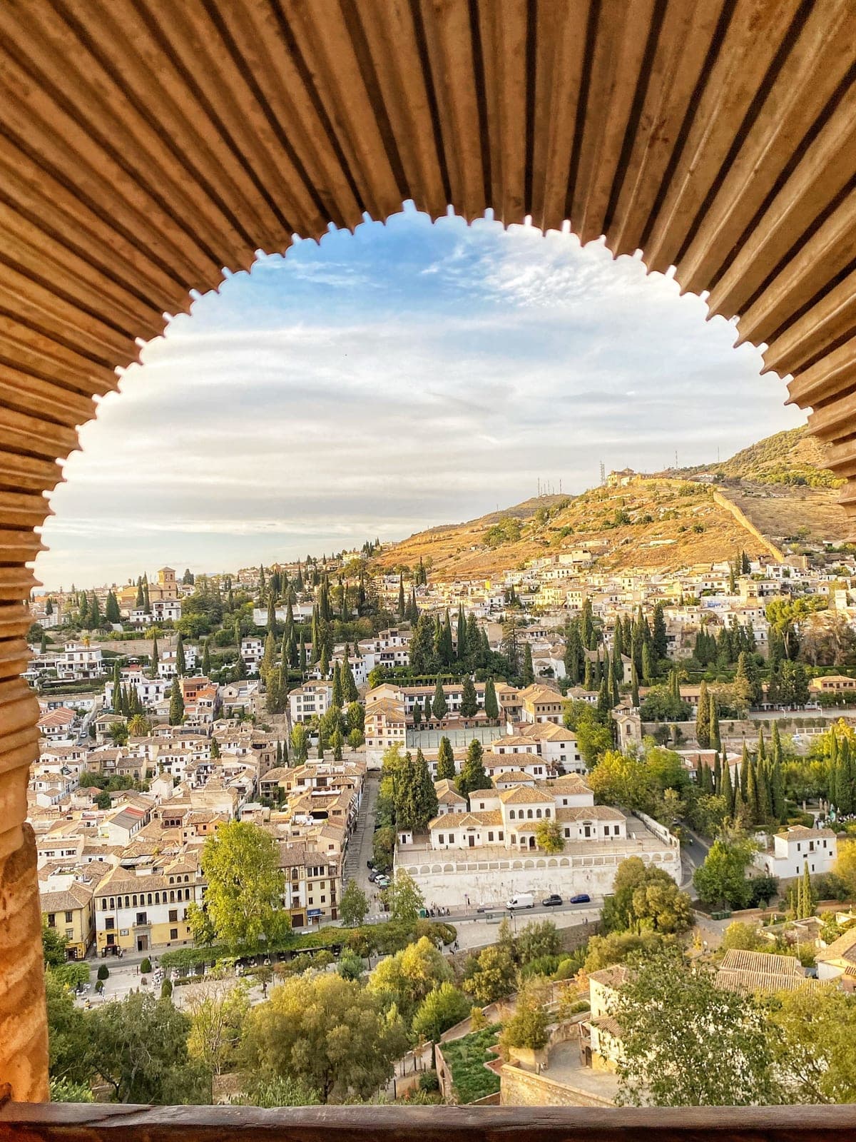 The whitewashed houses and gardens of the Albaicín quarter of Granada seen through a carved wooden arch, with the hillside behind