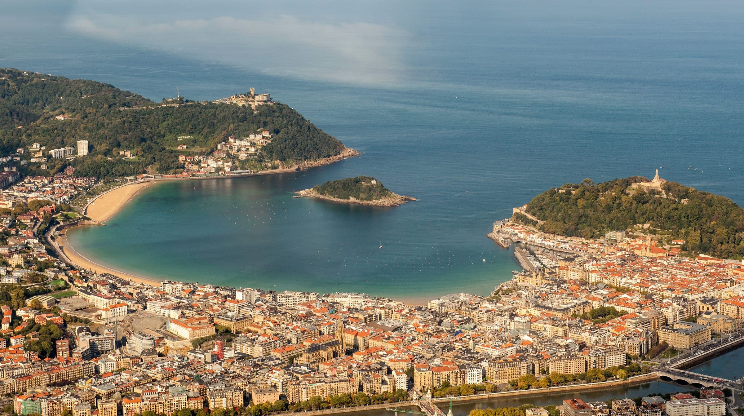 Aerial view of San Sebastián: La Concha bay and the island of Santa Clara between Monte Igueldo and Monte Urgull, with the Centro grid, the old town and the River Urumea in the foreground, the streets and seafront the marathon loops through