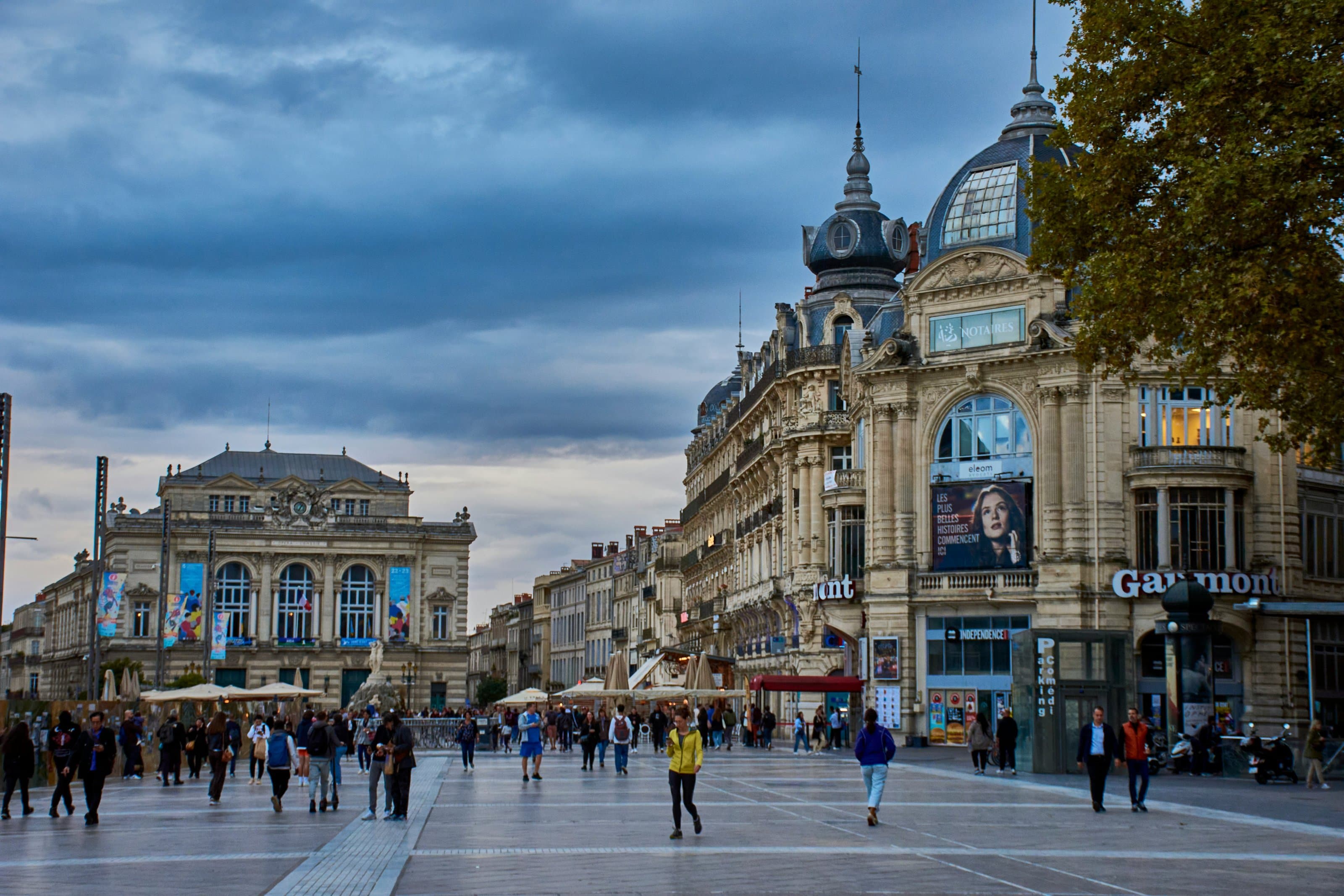 Place de la Comédie in Montpellier under a grey evening sky, with the Opéra Comédie on the left and domed 19th-century buildings on the right; the marathon crosses the square at km 3.5, 20.4 and 41.5