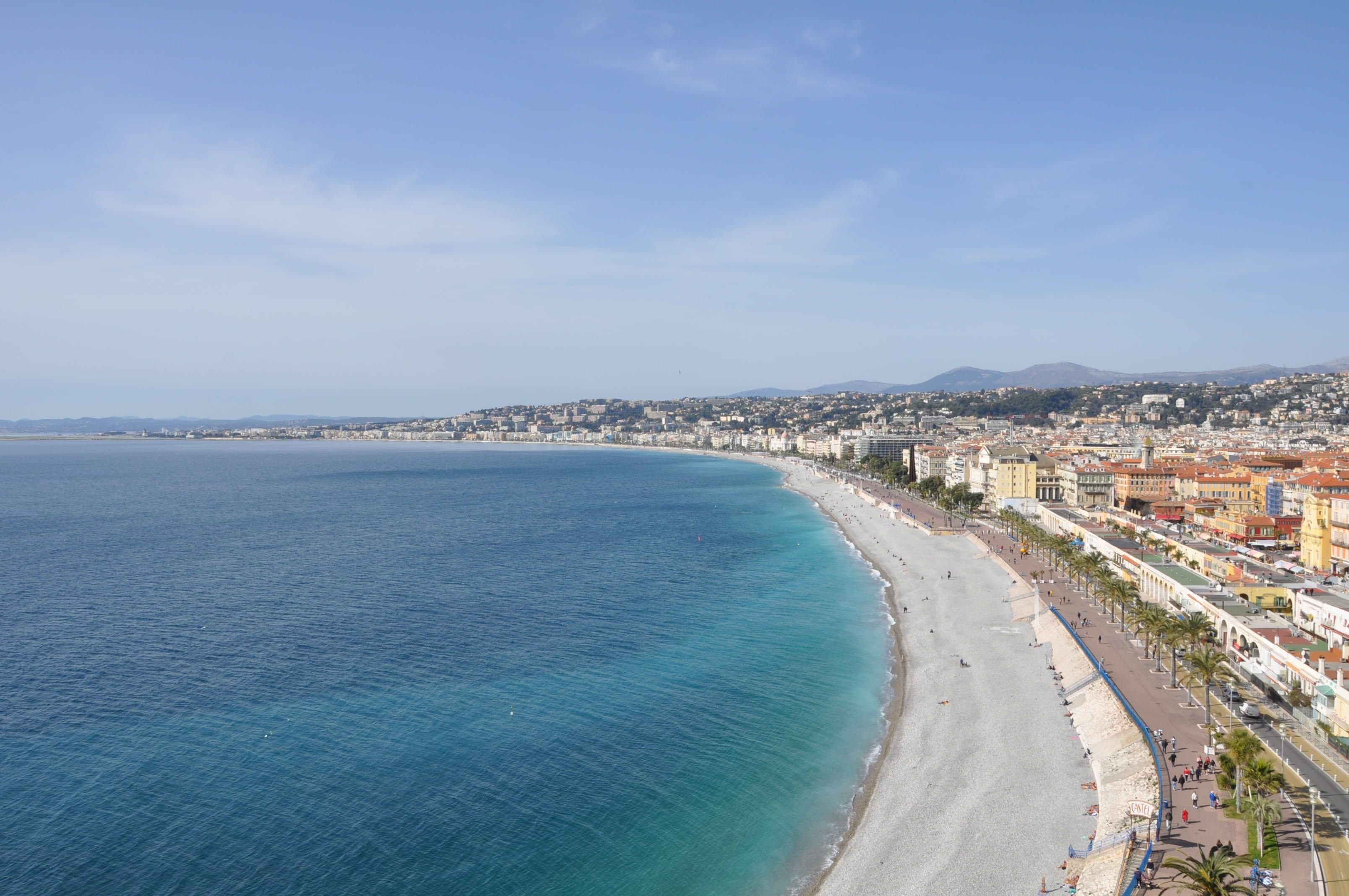 The Baie des Anges in Nice seen from above, with the pebble beach and the palm-lined Promenade des Anglais curving west towards the airport; the marathon starts on this promenade and follows it for the first 7 km