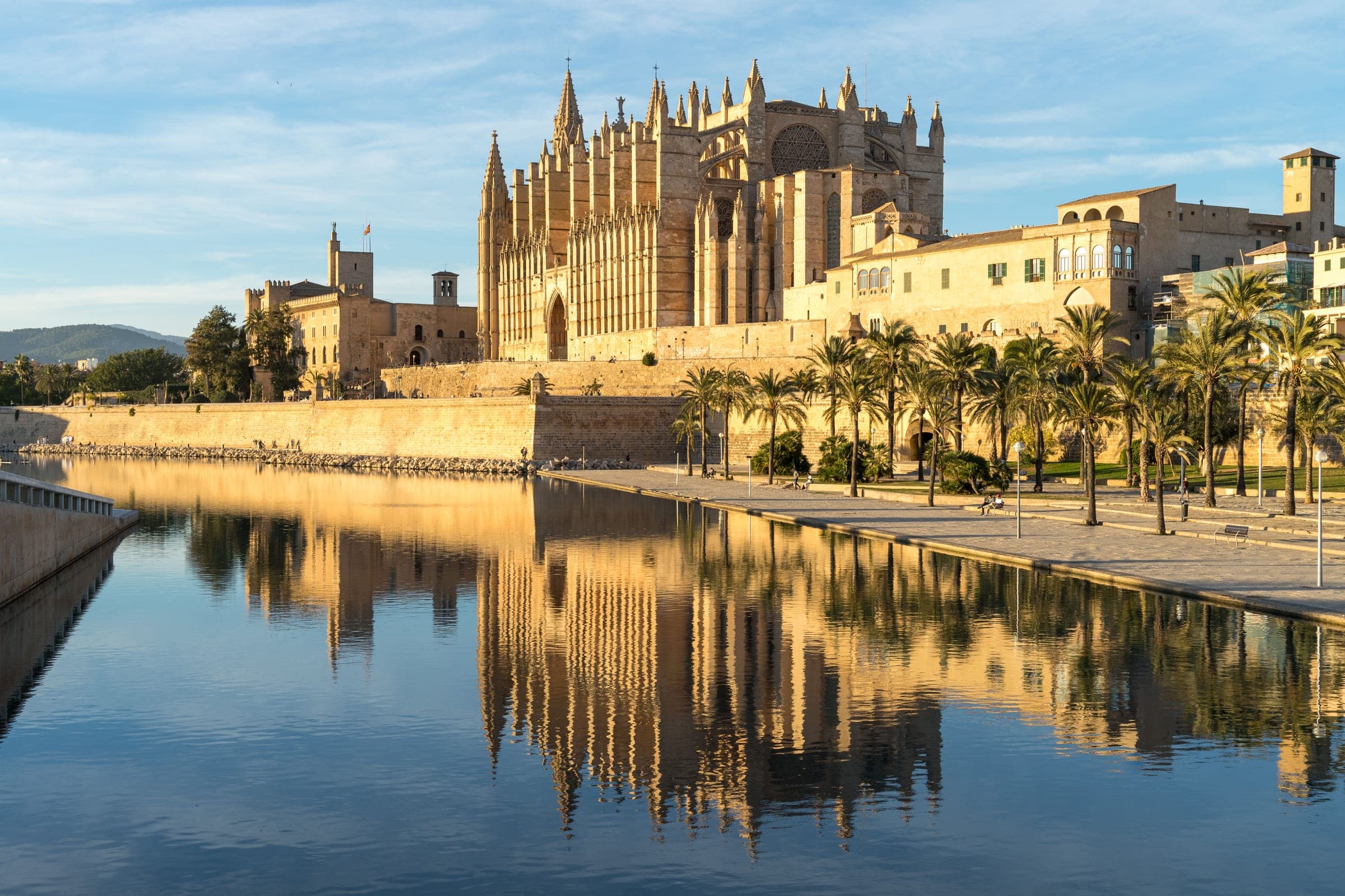 Palma Cathedral and the Almudaina palace above the old sea wall, reflected in the lake of Parc de la Mar in evening light, beside the marathon start and finish