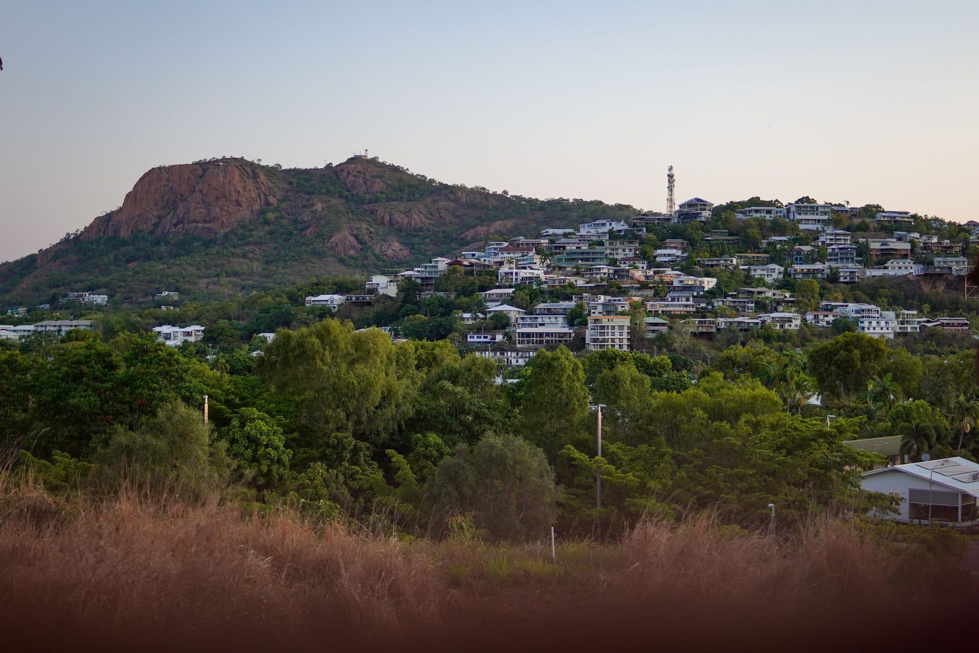 The red granite face of Castle Hill above hillside houses and trees in Townsville at dusk, about 1.5 km from the marathon start and finish at Jezzine Barracks