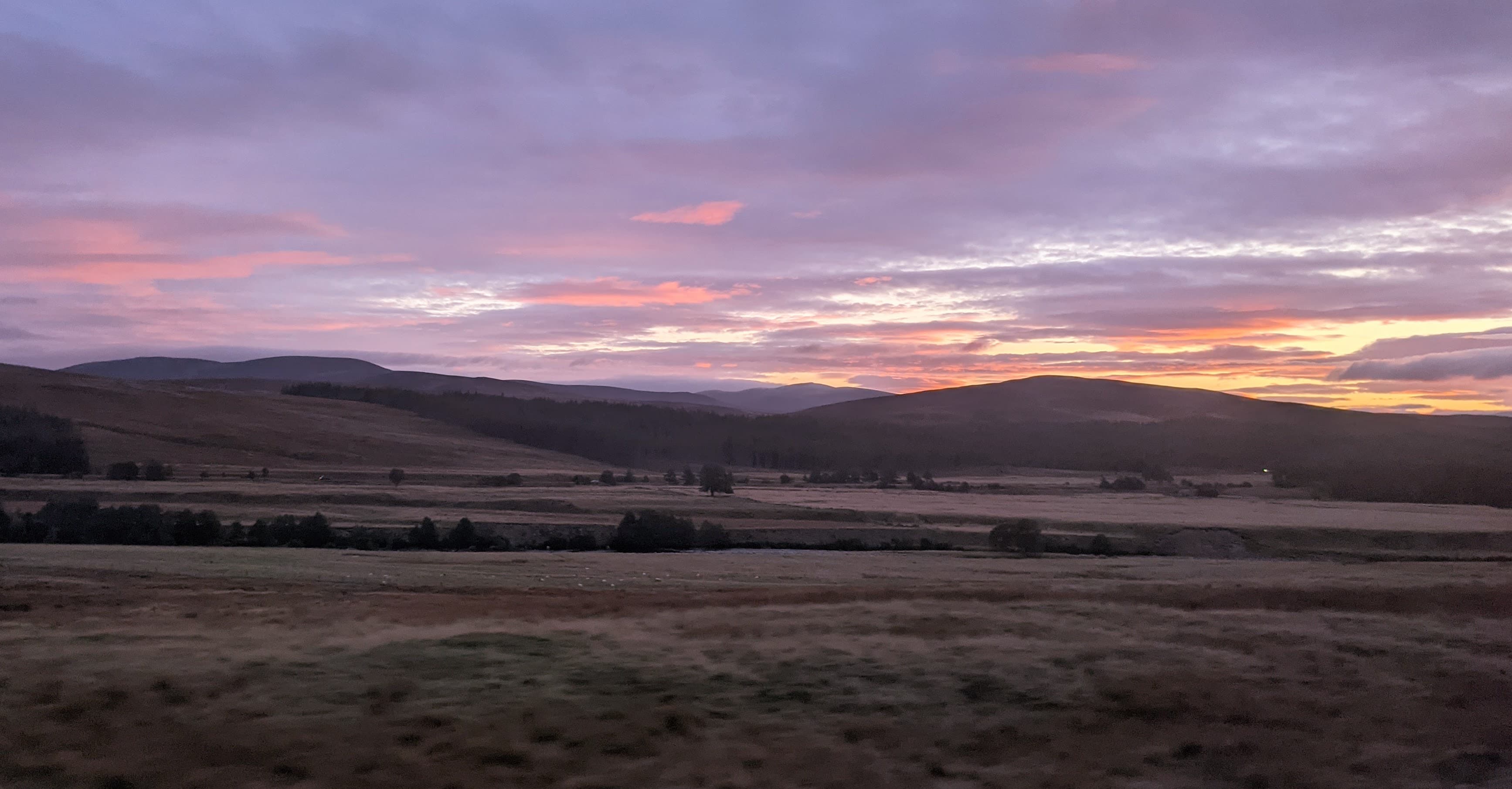 The Cairngorm plateau at dawn seen from a moving train window, the moorland turning pink under a still sky