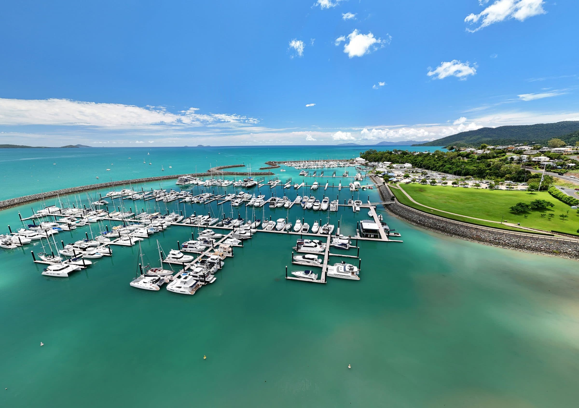 Aerial view of the Coral Sea Marina and the foreshore lawn at Airlie Beach, with the Whitsunday Islands on the horizon