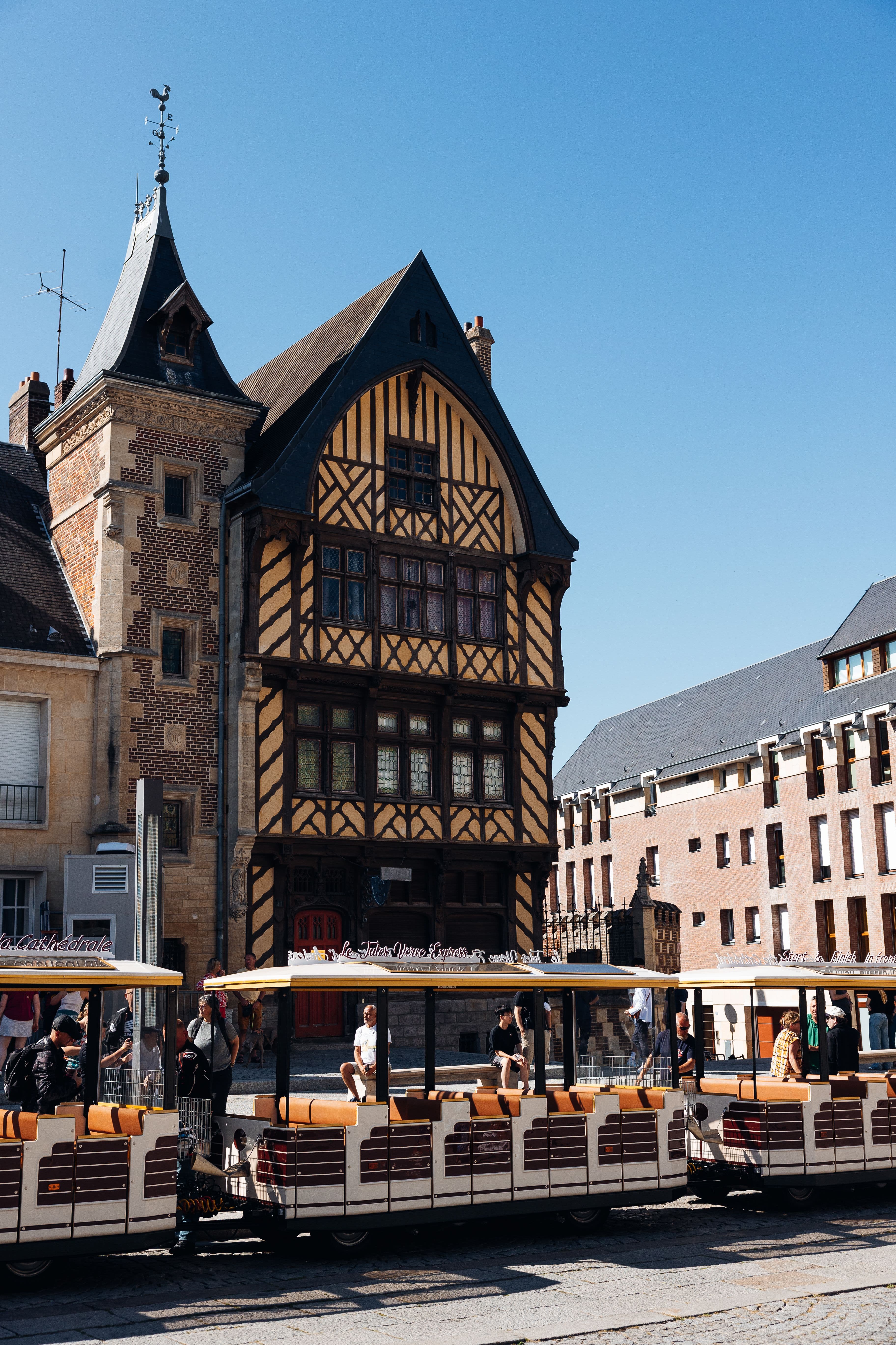 A tall half-timbered house with a brick corner tower in central Amiens, with the town's little tourist train passing in front. Central Amiens is about 4 km from the marathon's start and finish.