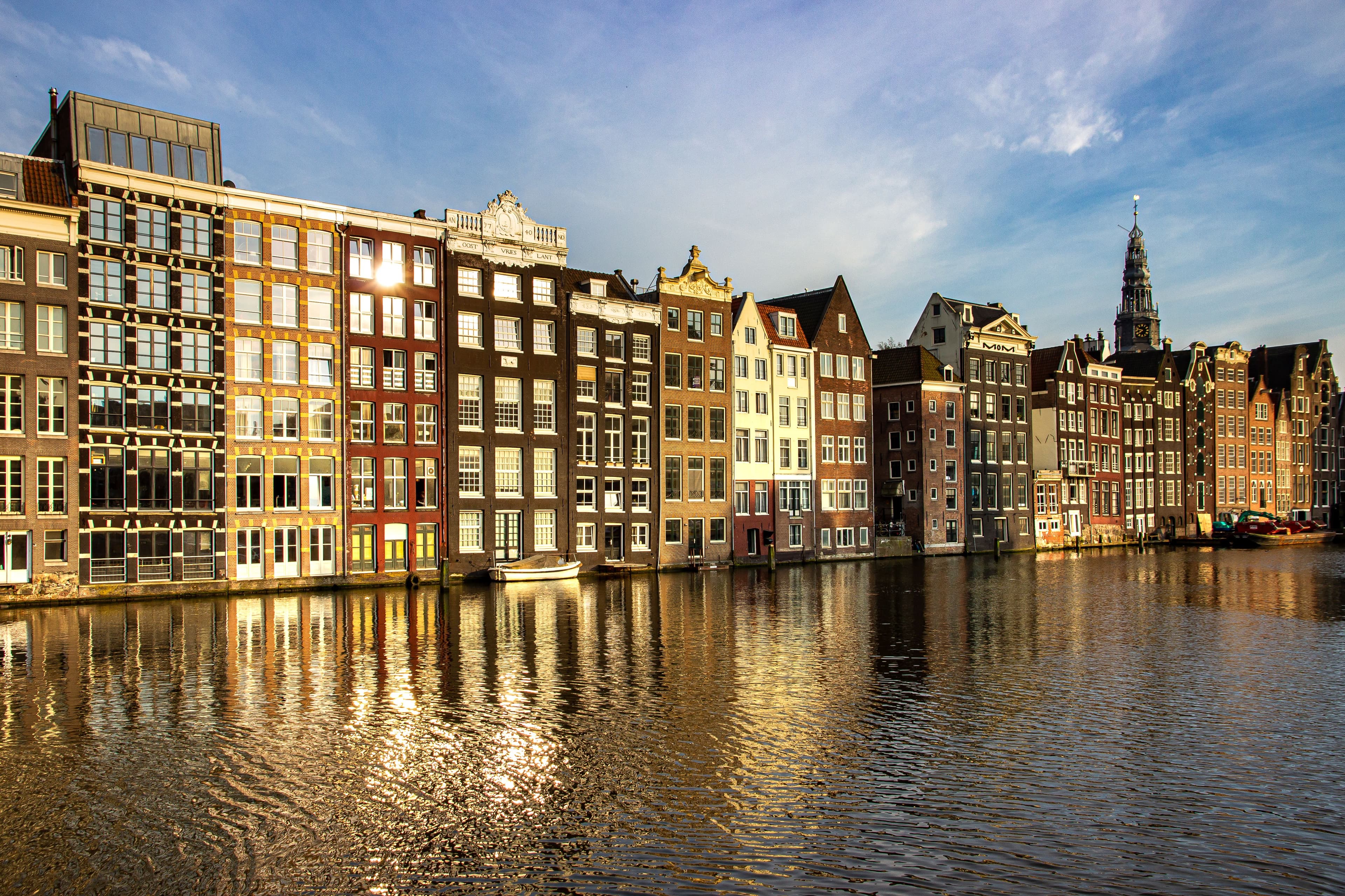 Canal houses reflected in an Amsterdam canal at golden hour, near the Damrak in central Amsterdam