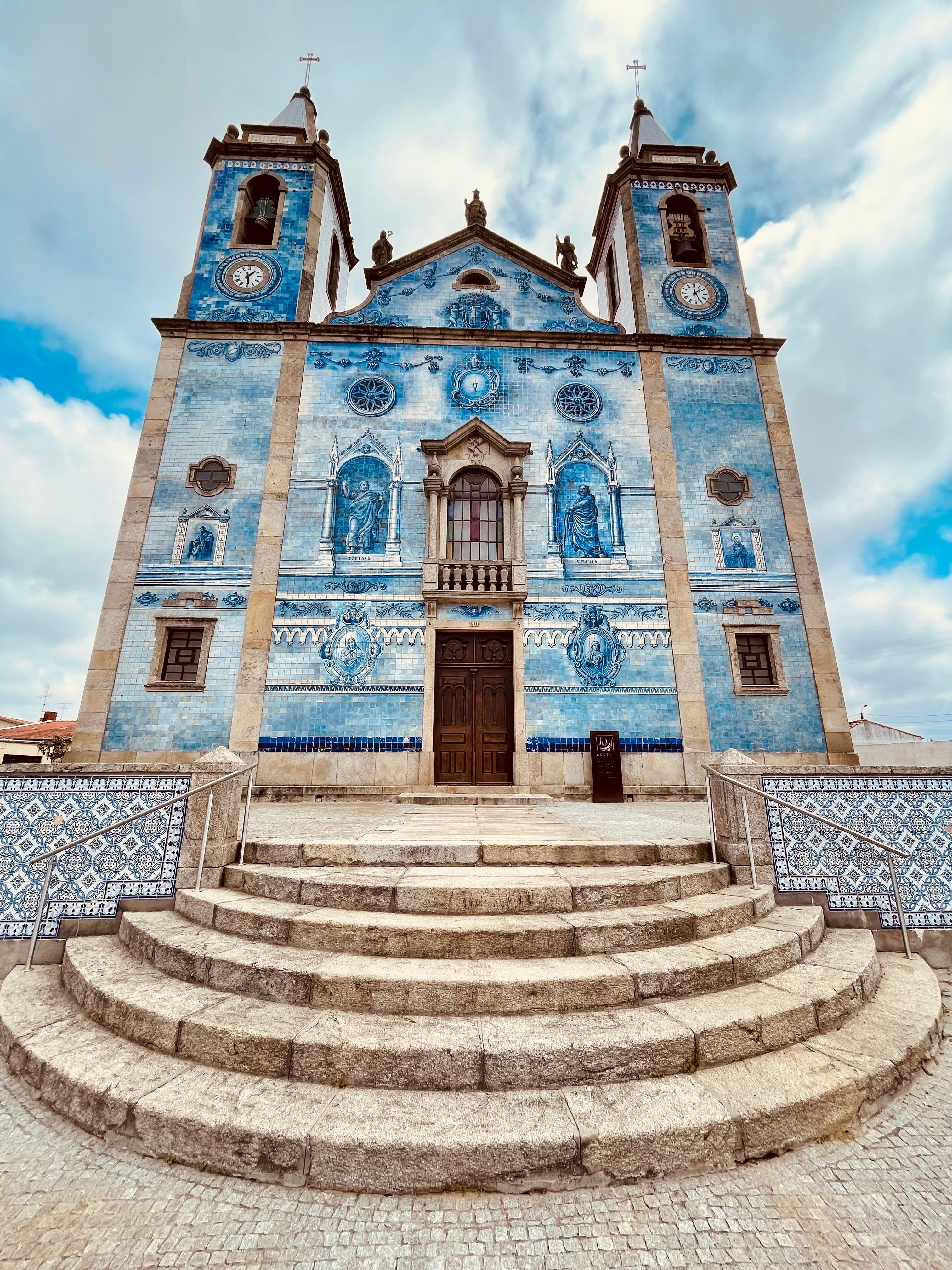 A twin-towered church faced entirely in blue and white azulejo tiles, with stone steps and tiled walls in front, in the Aveiro region the marathon course crosses
