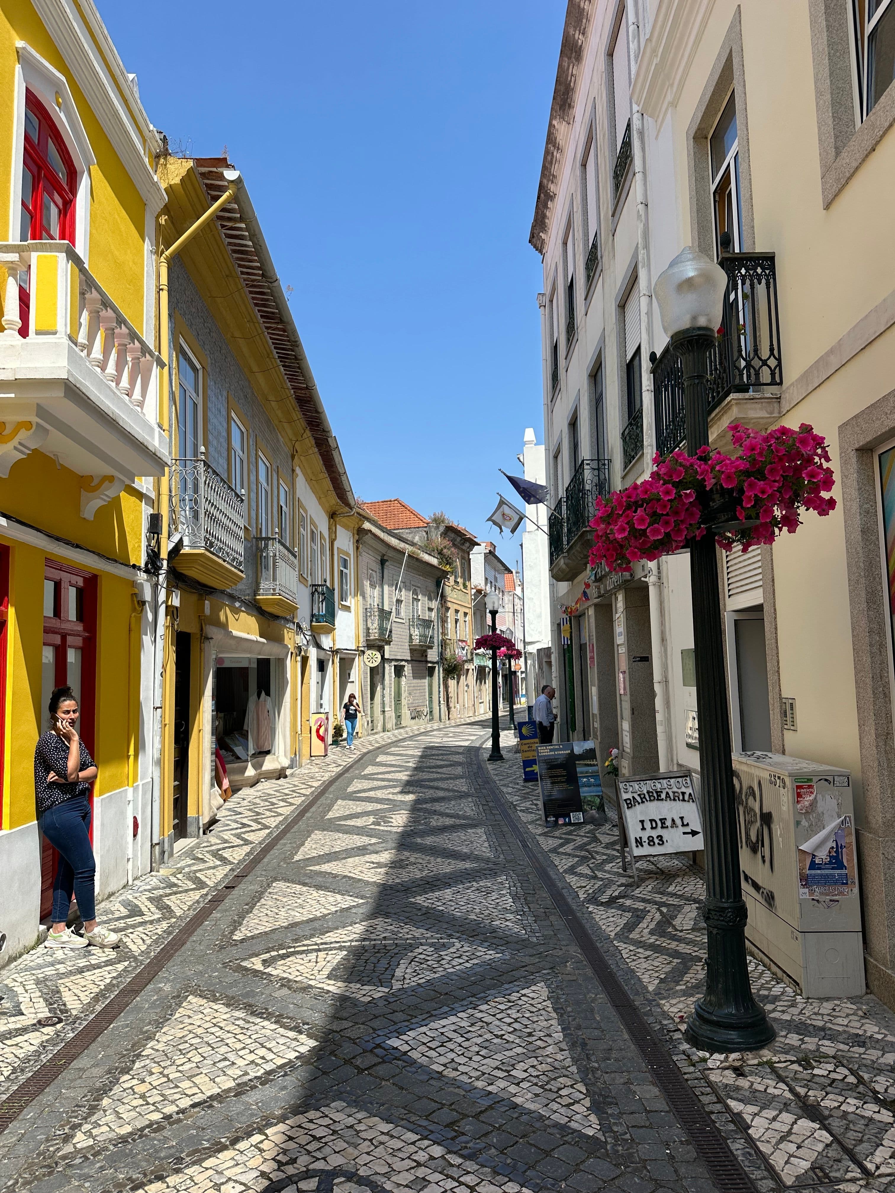 A narrow Aveiro shopping street with patterned calçada paving, yellow and tiled houses and wrought-iron balconies, in the city centre the marathon runs through in its opening kilometres