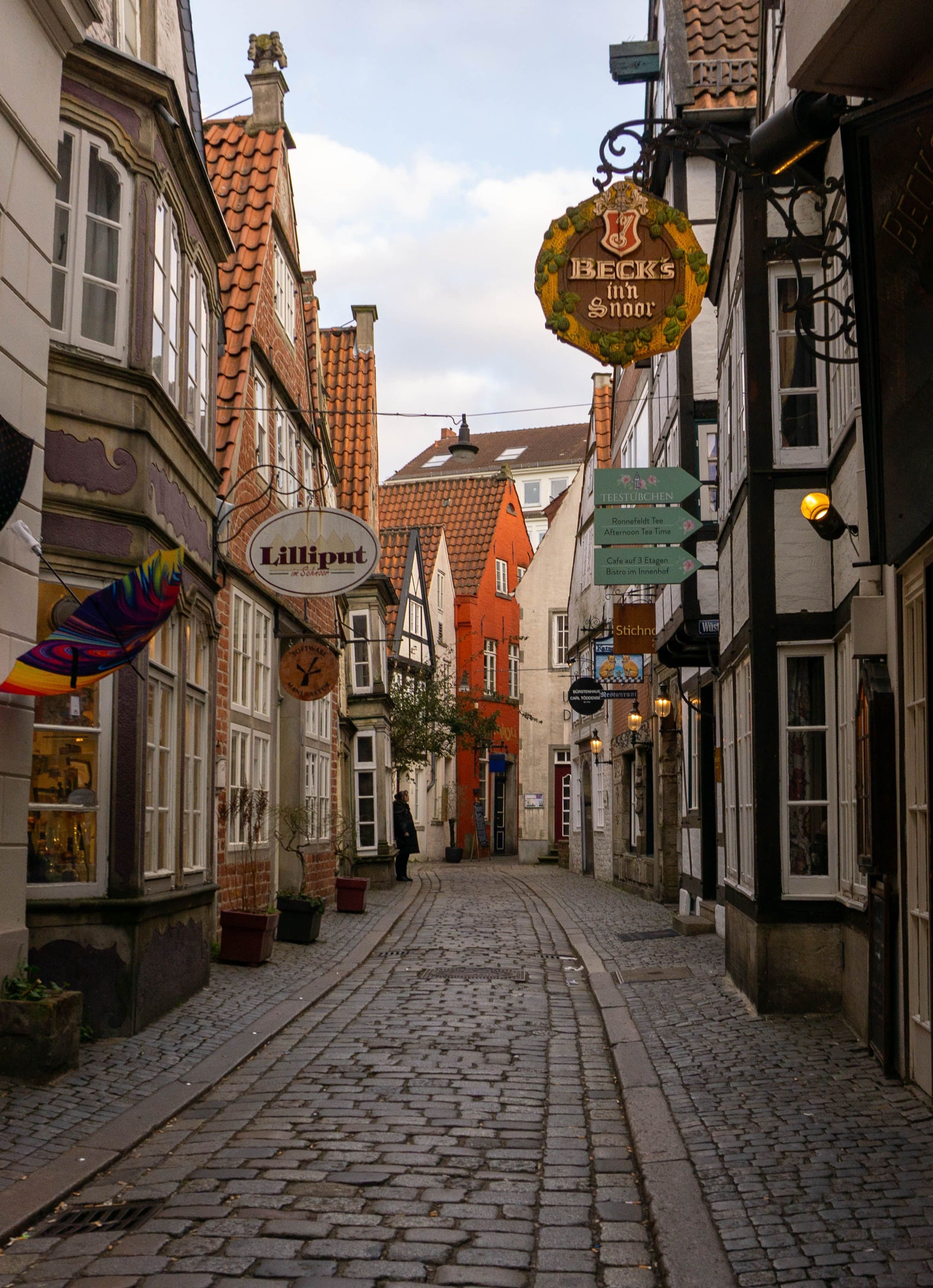 A narrow cobbled lane in Bremen's Schnoor quarter lined with leaning gabled houses and hanging shop signs, the medieval district a few minutes' walk from the marathon finish