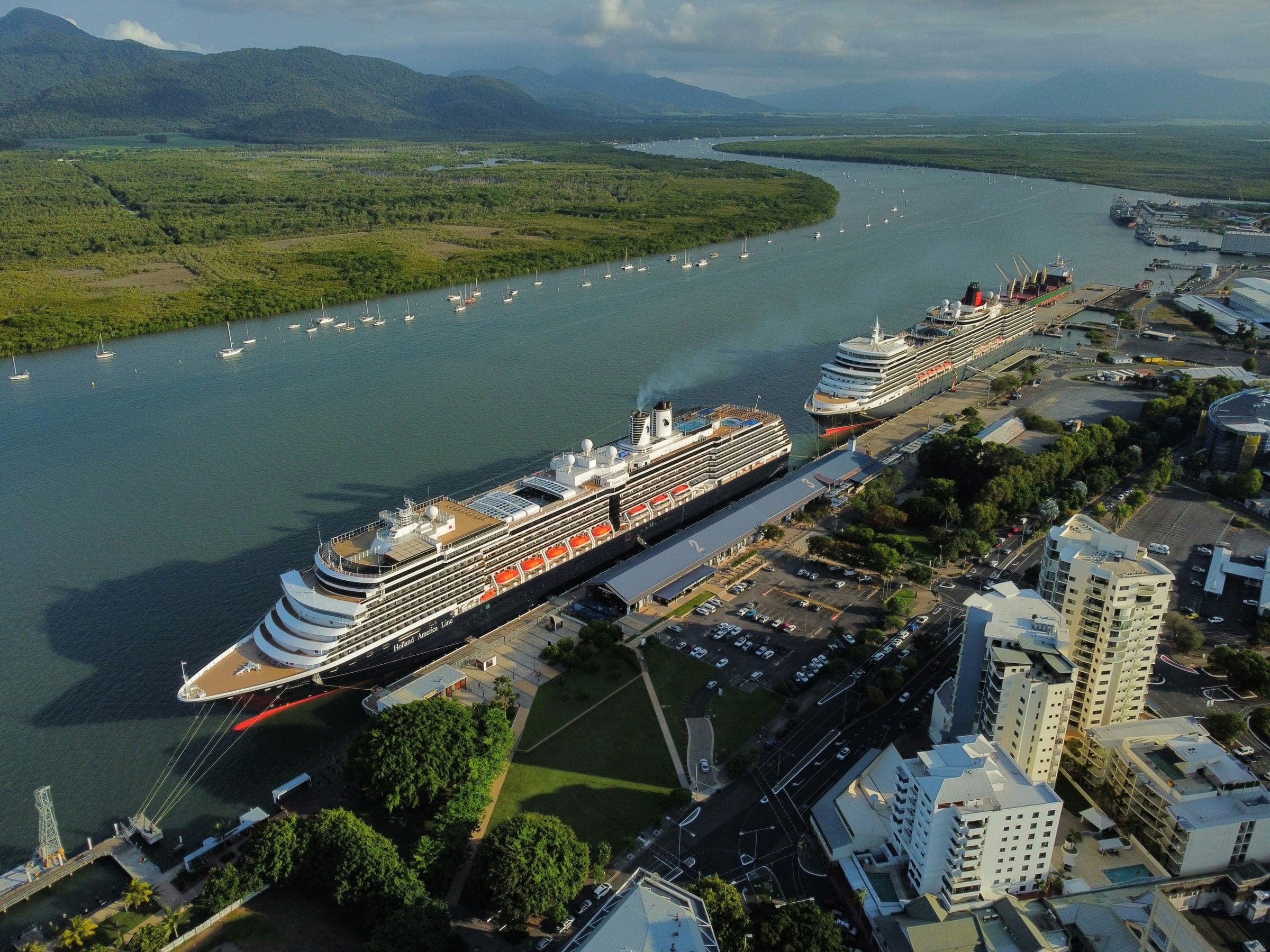 Aerial view of two cruise ships at the Cairns cruise terminal on Trinity Inlet, with the city’s waterfront towers on the right and mangroves and rainforest-covered ranges behind