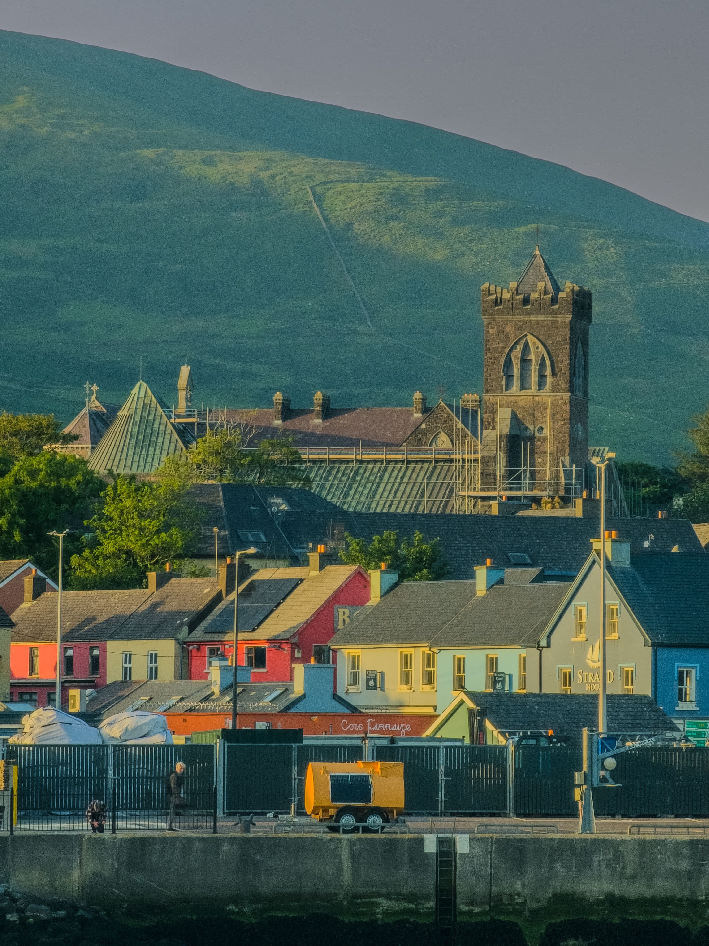 Dingle town's harbourside houses and St James's Church tower at sunset, with the Slieve Mish mountains behind
