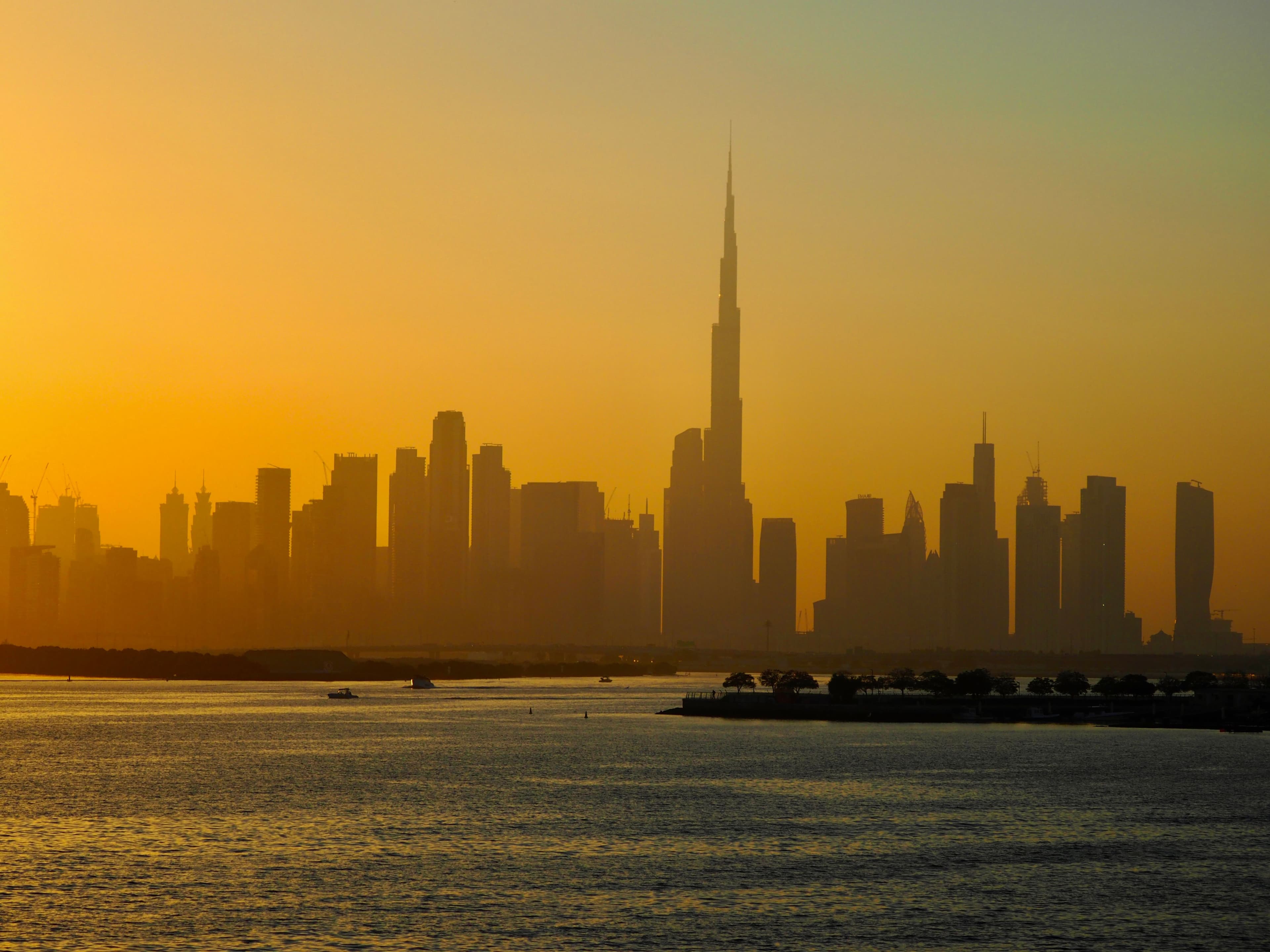 Dubai skyline and Burj Khalifa silhouetted at sunset, viewed across the water