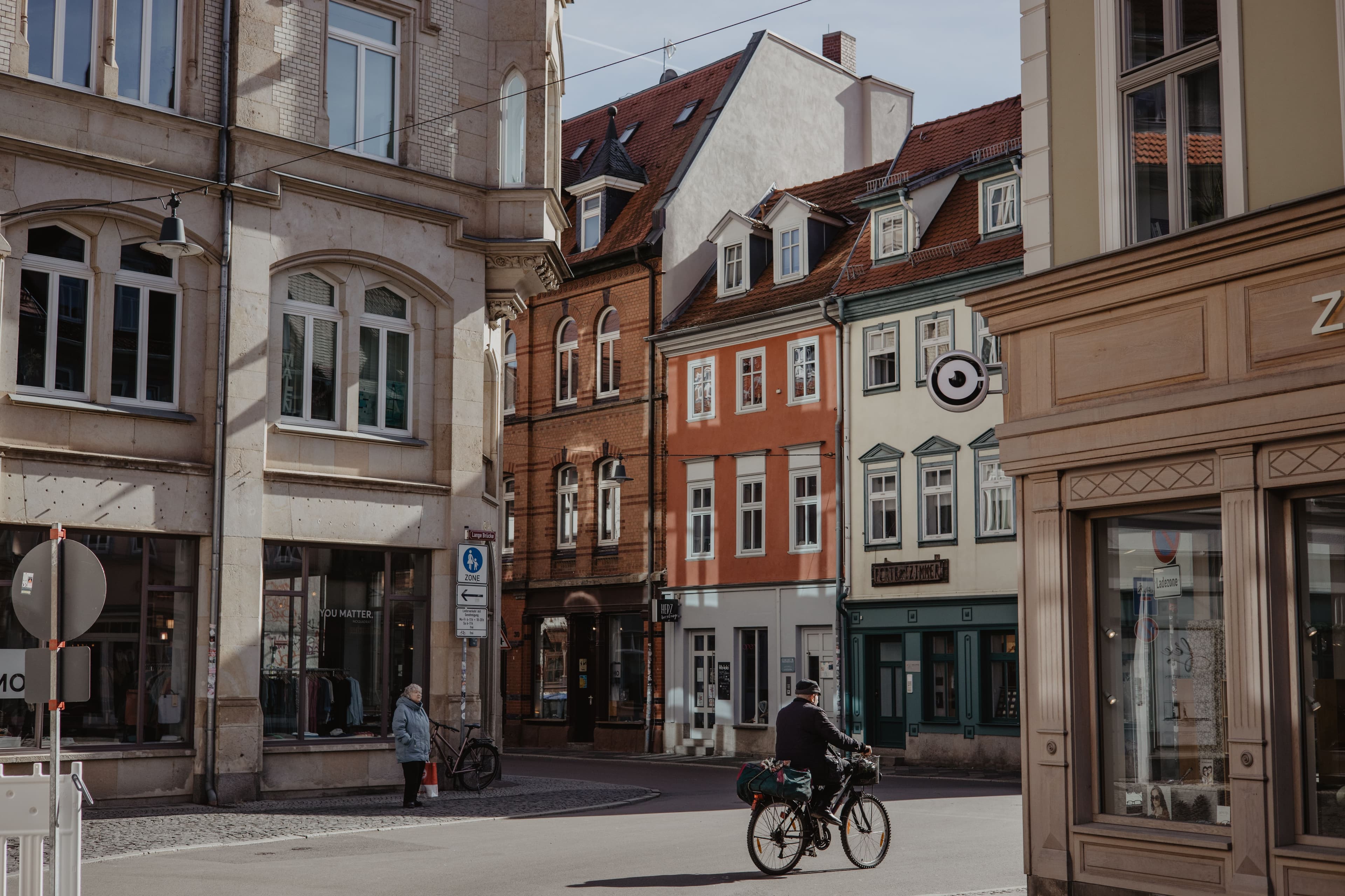A quiet street corner in Erfurt's old town by the Lange Brücke sign, with shopfronts under gabled and half-timbered buildings and a cyclist crossing the cobbles