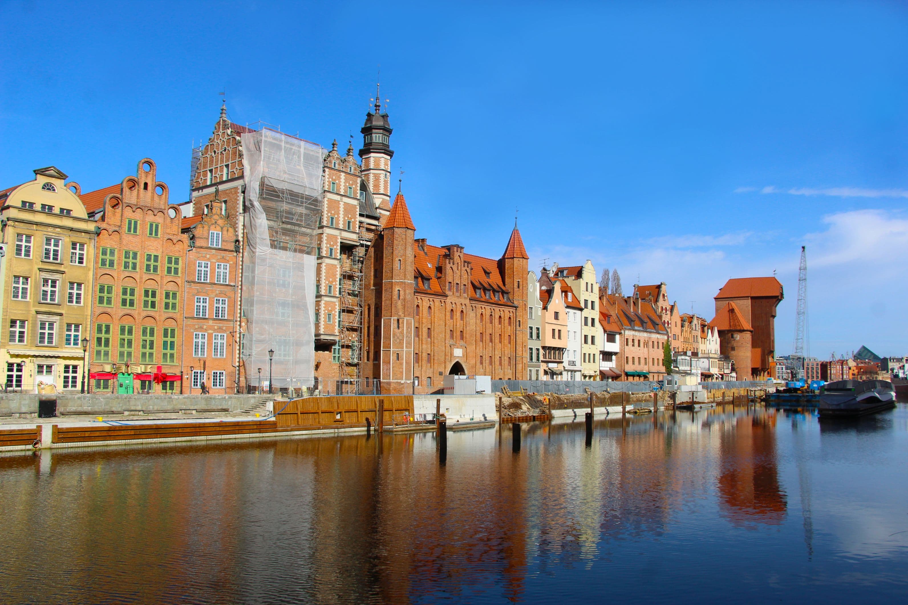 Gabled Hanseatic merchant houses reflected in the Motława river, Gdańsk Old Town, with the medieval Gdańsk Crane in the distance
