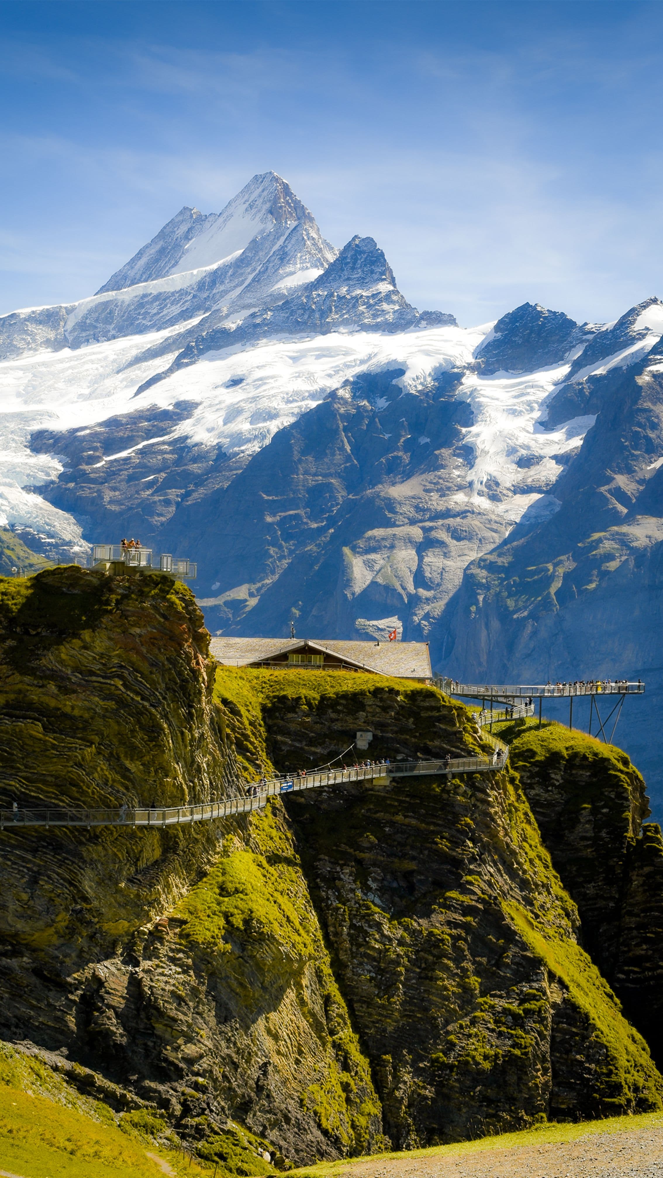 Snow-capped Bernese Oberland peaks and glaciers viewed from a cliff-edge walkway near Grindelwald, beneath the mountains the marathon finishes below
