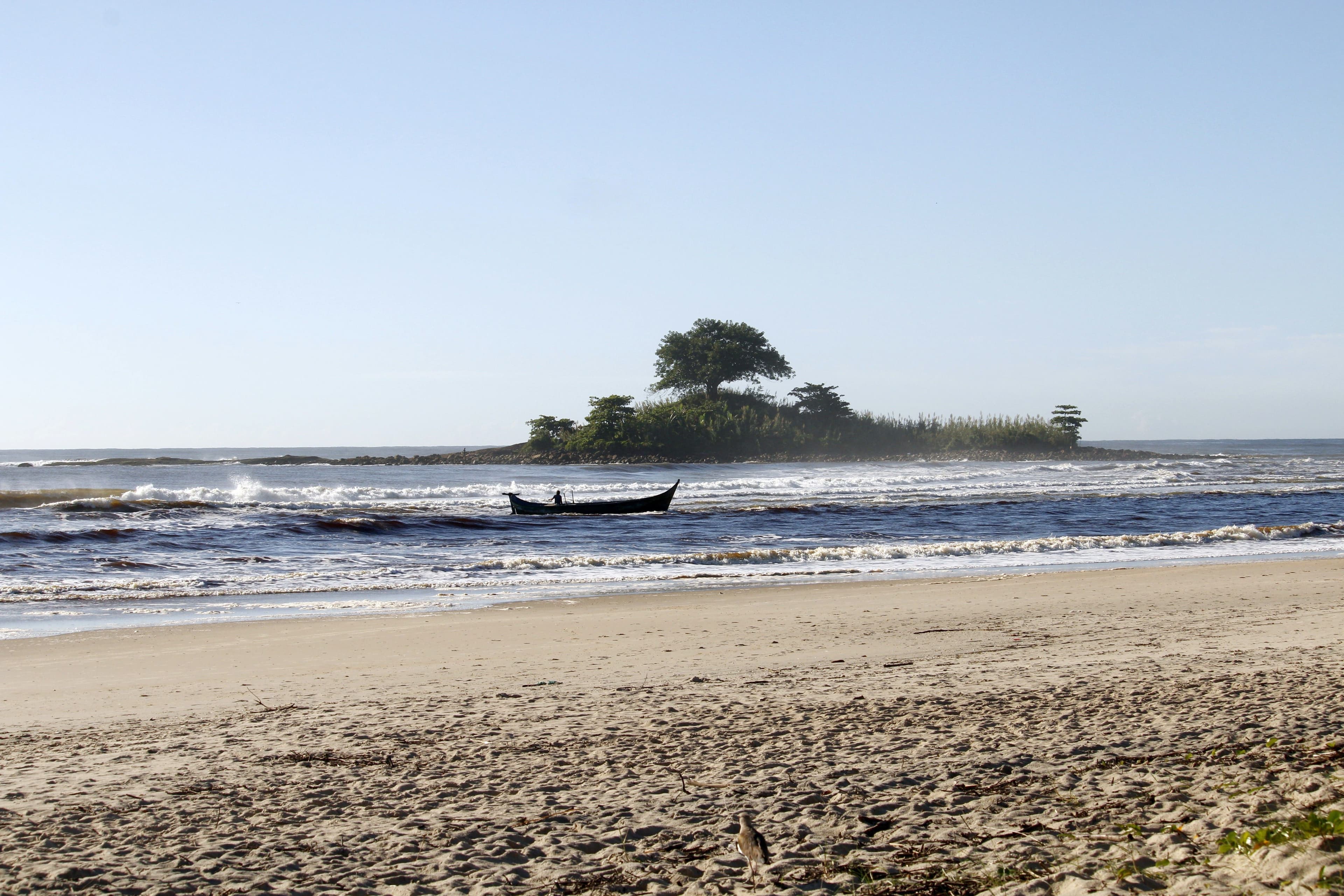 A small wooded islet in calm water off the Paraná coast at Guaratuba, with a fishing canoe in the foreground