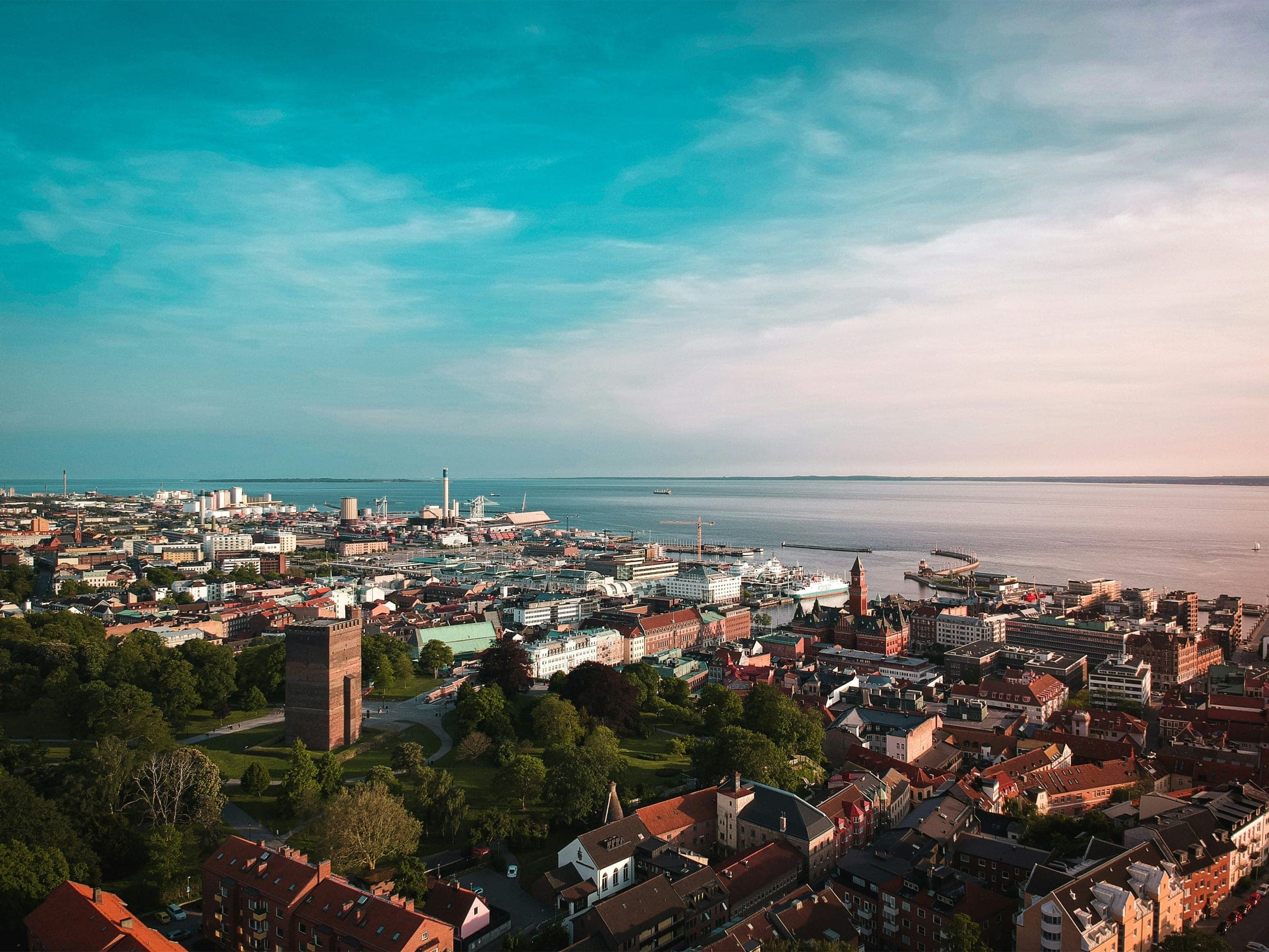 Aerial view of Helsingborg at sunset, with the brick Kärnan tower in the park on the hill, the town hall tower, the harbour and ferries on the Öresund