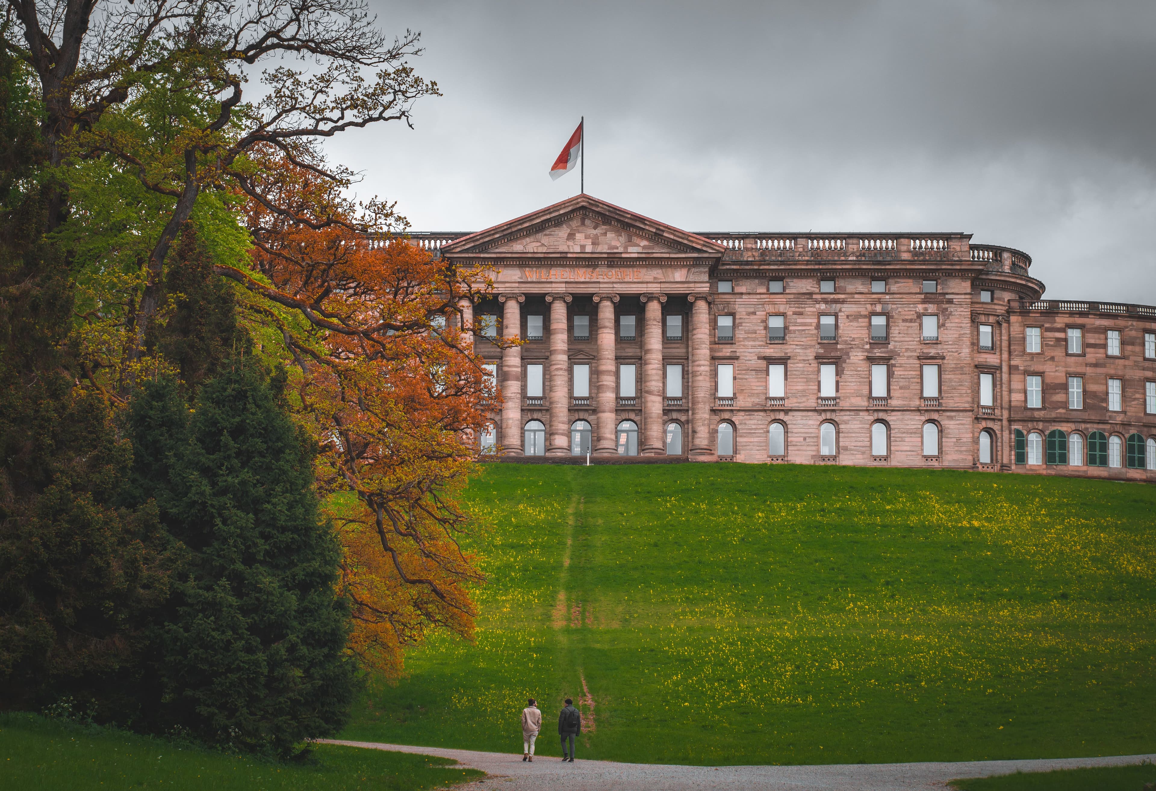 Schloss Wilhelmshöhe above its meadow in Bergpark Wilhelmshöhe, Kassel, under autumn cloud. The marathon climbs toward this western side of the city on each lap but stops short of the park.