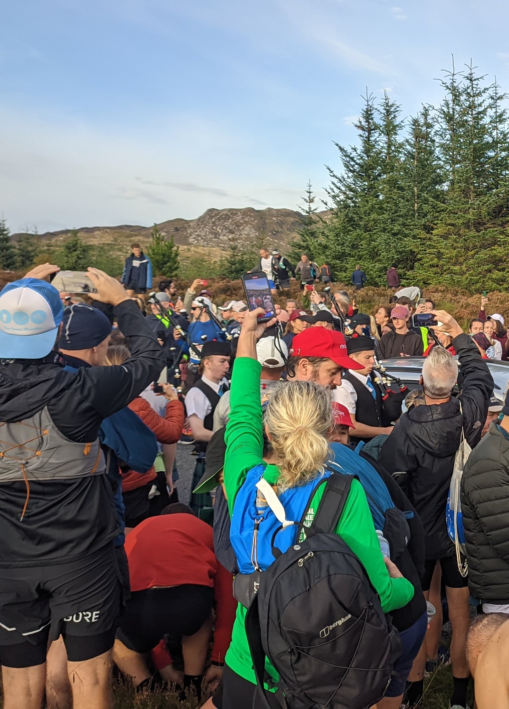 Bagpipers and runners gathered at the remote Loch Ness Marathon start line on the South Loch Ness road, hills and forestry visible behind
