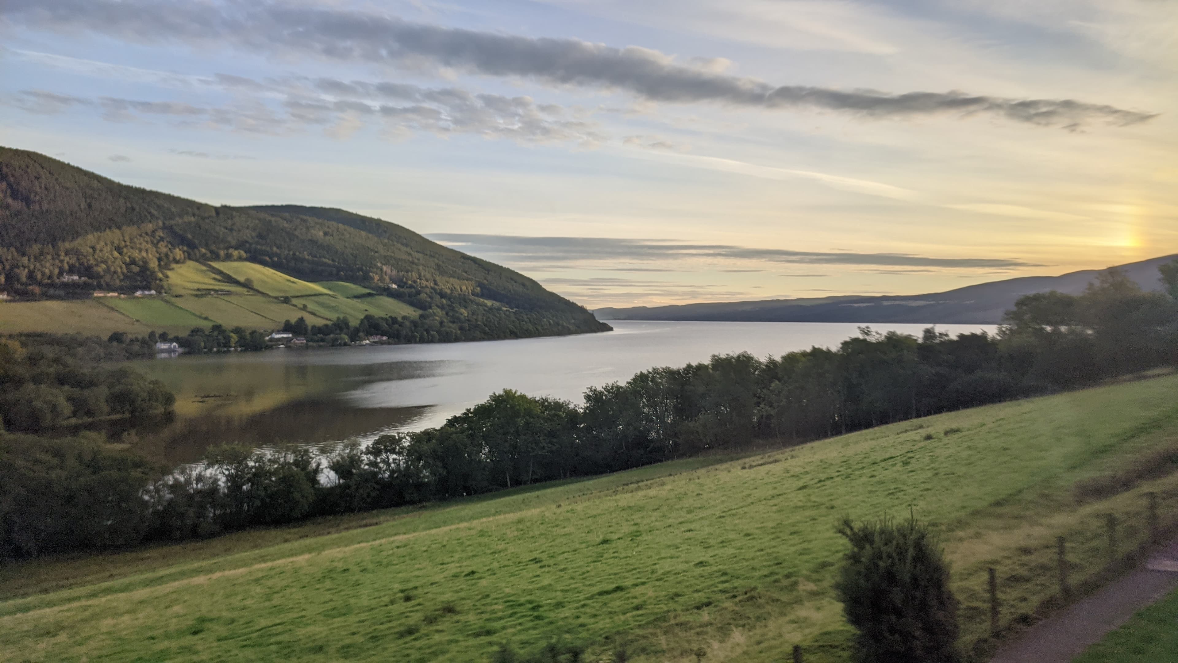 Loch Ness at golden hour, viewed from the hillside above the south shore near the marathon route, with wooded hills framing the water