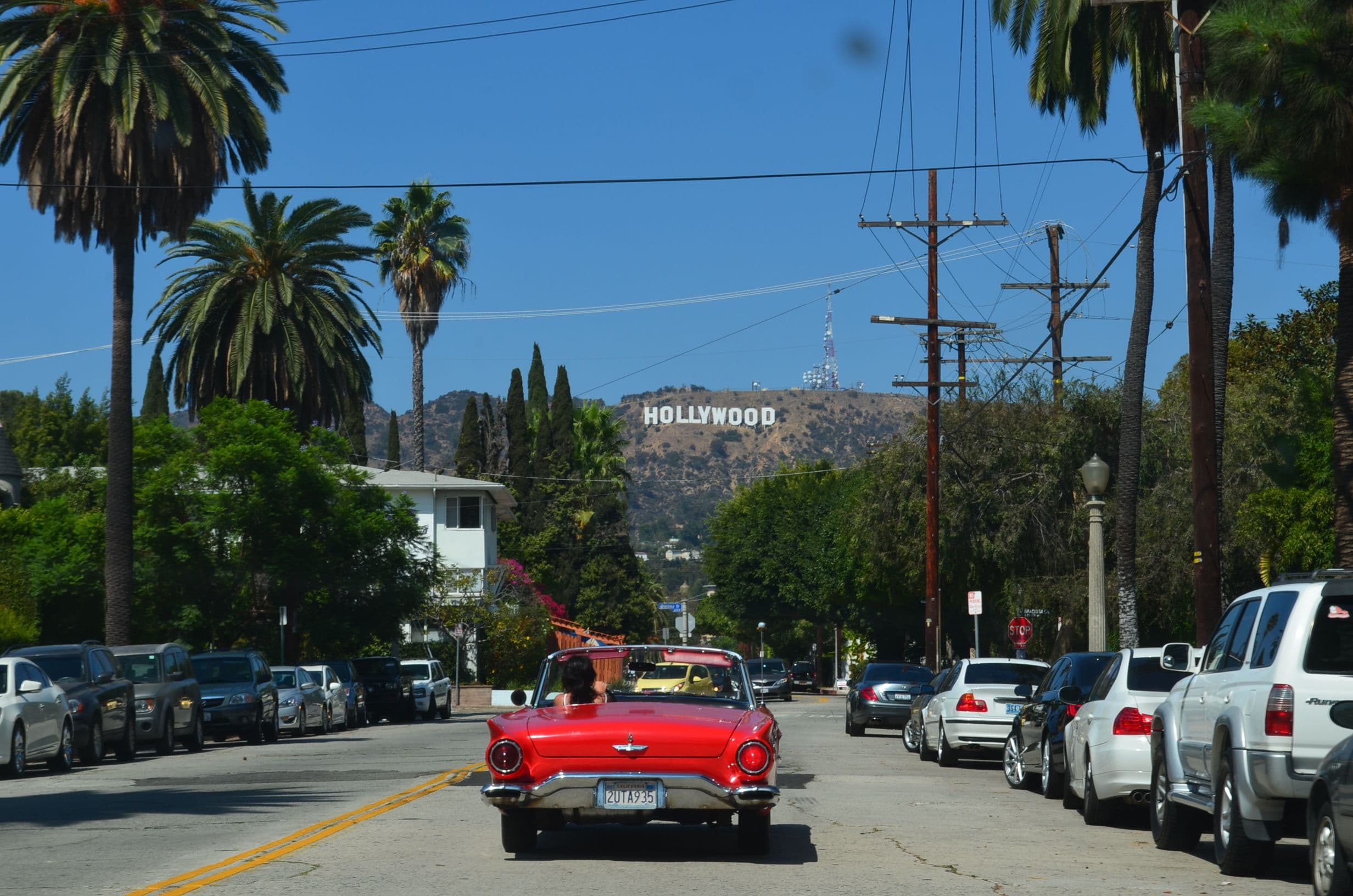 A classic convertible on a palm-lined Los Angeles street with the Hollywood sign visible in the hills, on the marathon's Hollywood Boulevard stretch