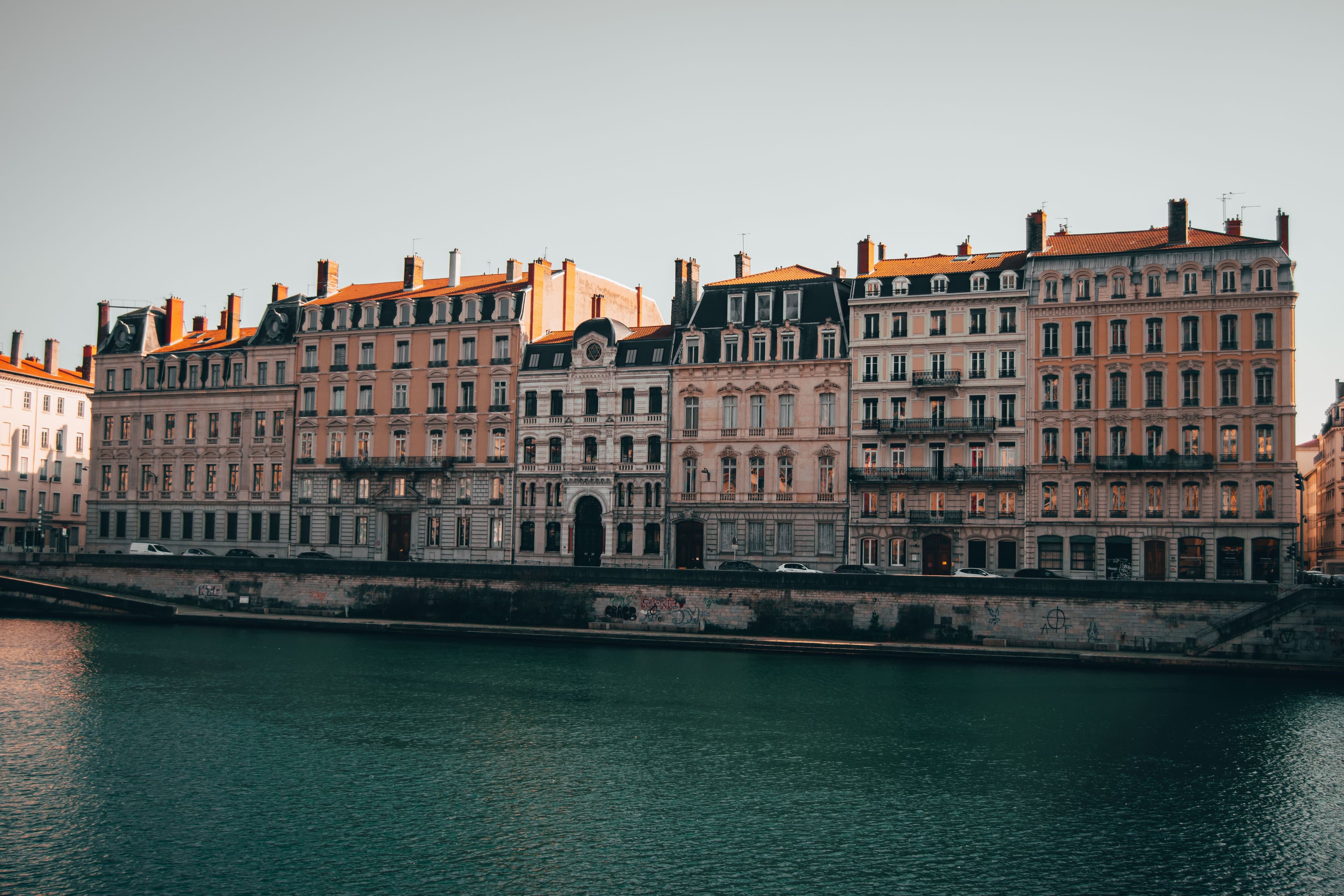 Nineteenth-century apartment buildings along Quai Tilsitt on the Saône in Lyon, including the facade of the Grand Synagogue, with the stone river wall below. The marathon finishes a few hundred metres away at Place Bellecour.