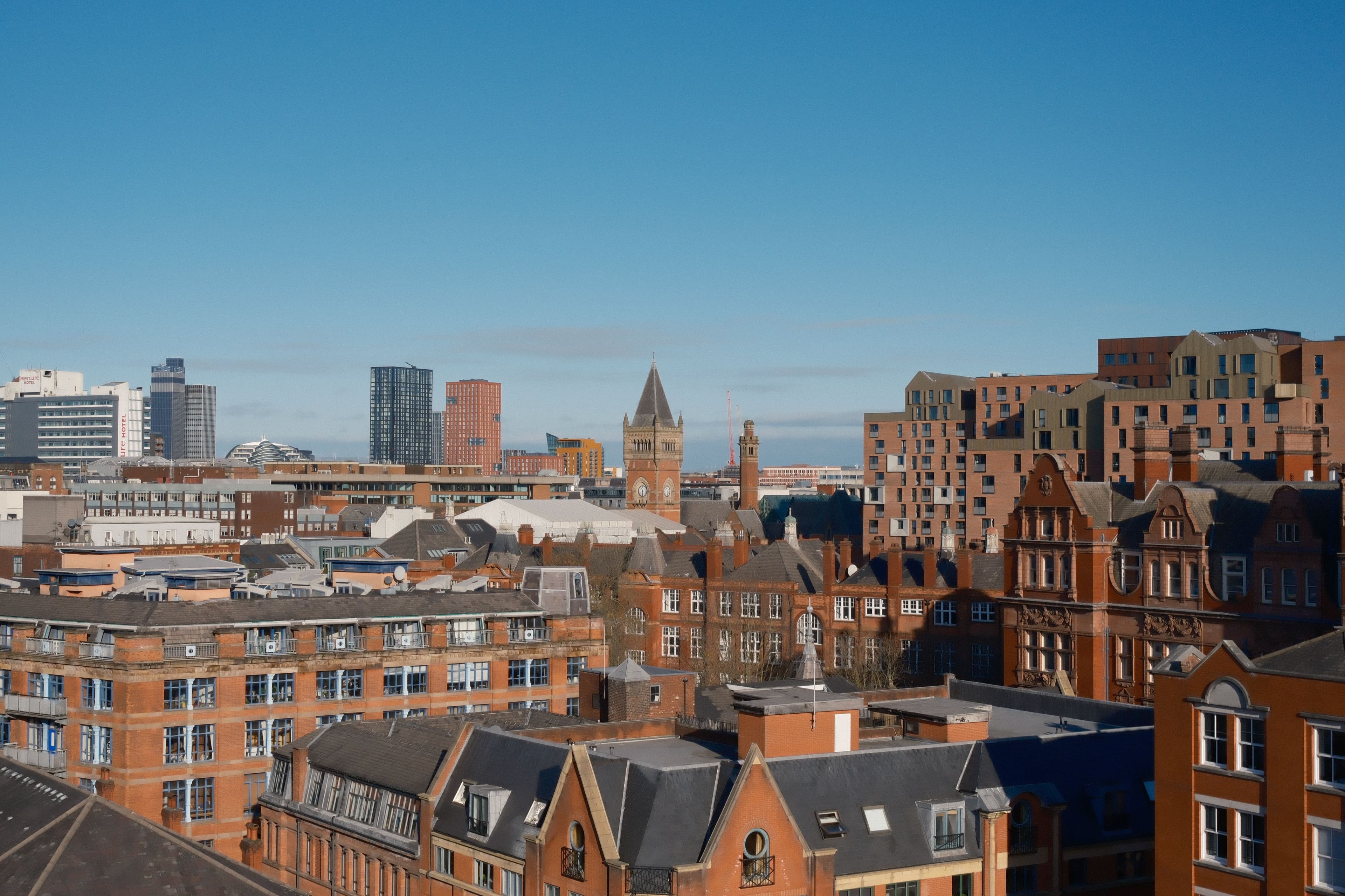 Manchester city centre skyline of red-brick Victorian buildings and a clock tower, with modern high-rises behind, close to the marathon's opening city-centre miles