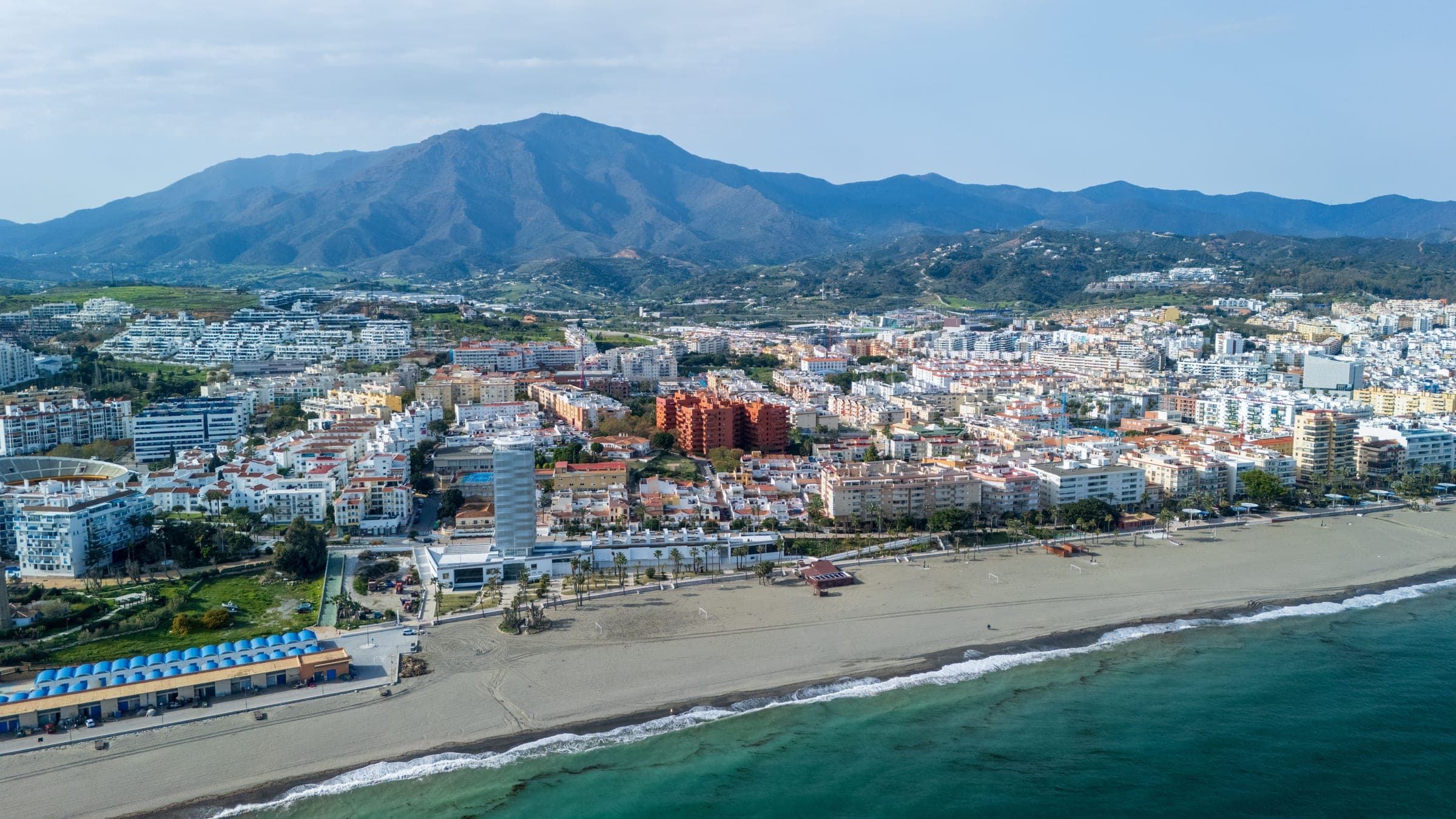 Aerial view of Estepona’s seafront and beach with the whitewashed town behind and the Sierra Bermeja rising above it, the shore the marathon follows east and west