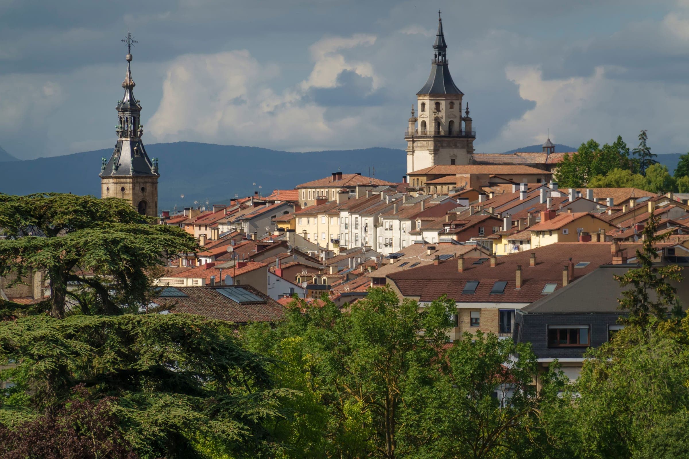 The tiled roofs of Vitoria-Gasteiz’s medieval quarter rising to the tower of Santa María Cathedral and the spire of San Pedro, with the green hills of Álava behind, the old town the marathon circles at km 18
