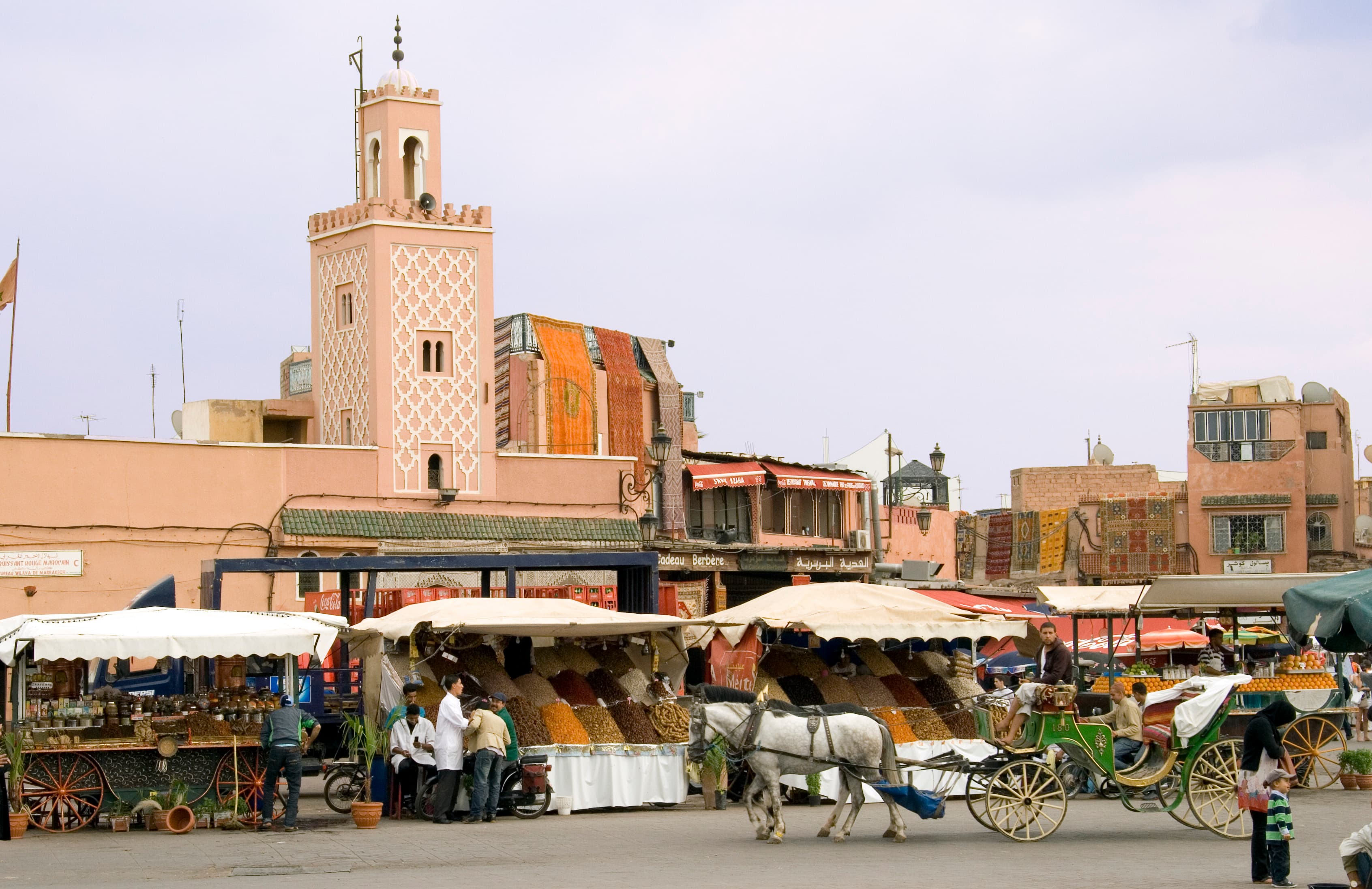 Jemaa el-Fna square in Marrakech, Morocco, with market stalls, a horse-drawn carriage and the Koutoubia-style minaret behind, close to the Marrakech Marathon's Marathon Village