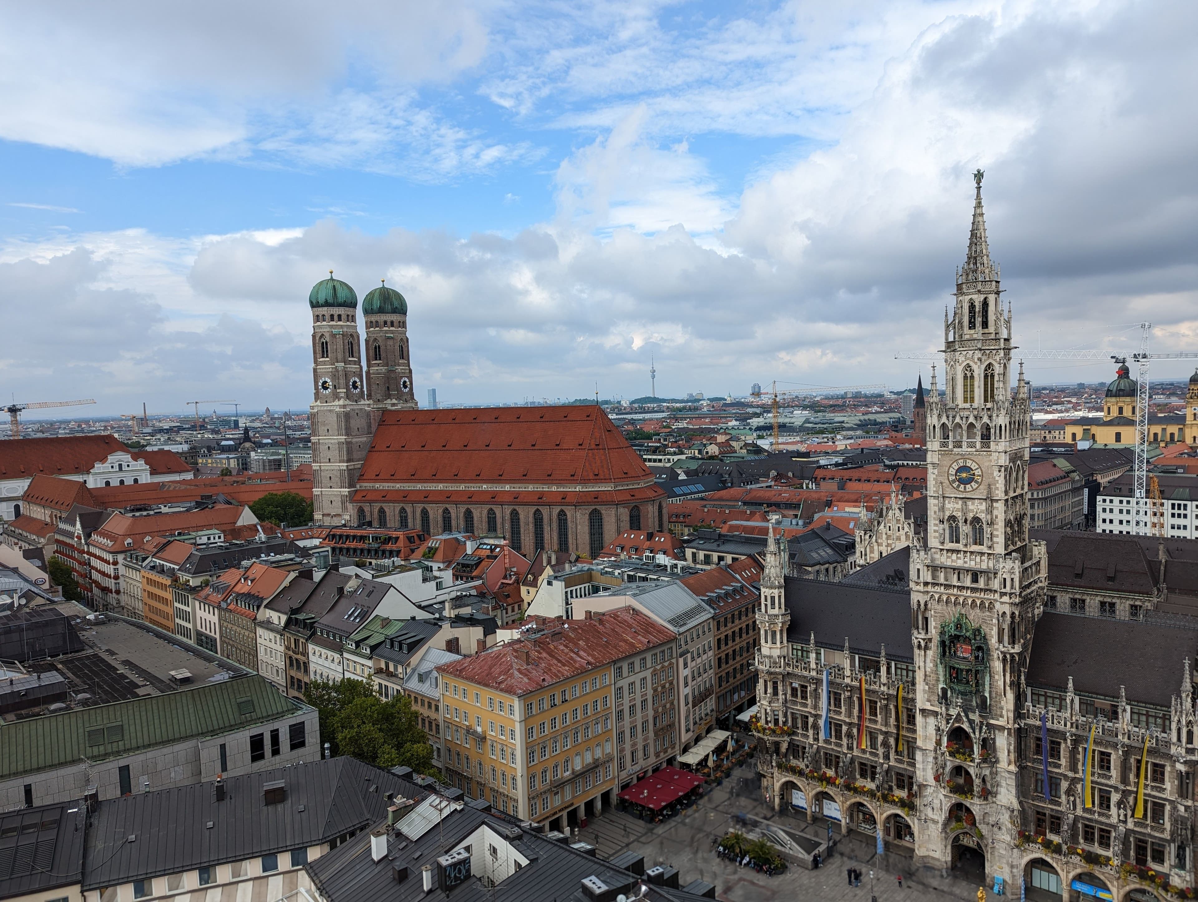 Munich's old town from above, with the Neues Rathaus clock tower on the right and the twin onion domes of the Frauenkirche beyond. The marathon runs through Marienplatz below, passing this square three times.