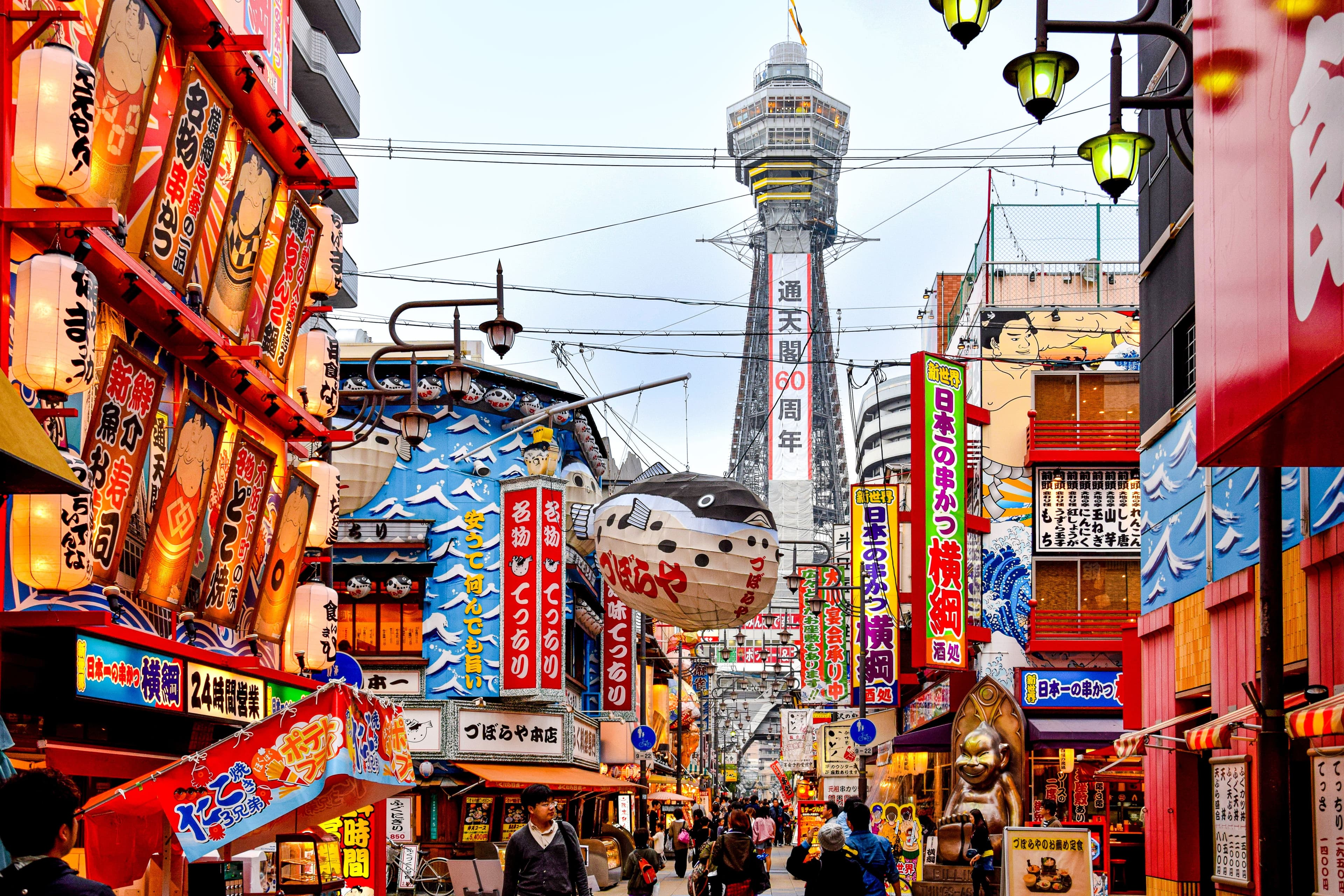 The neon-lit Shinsekai district in Osaka, with Tsutenkaku Tower rising above the street