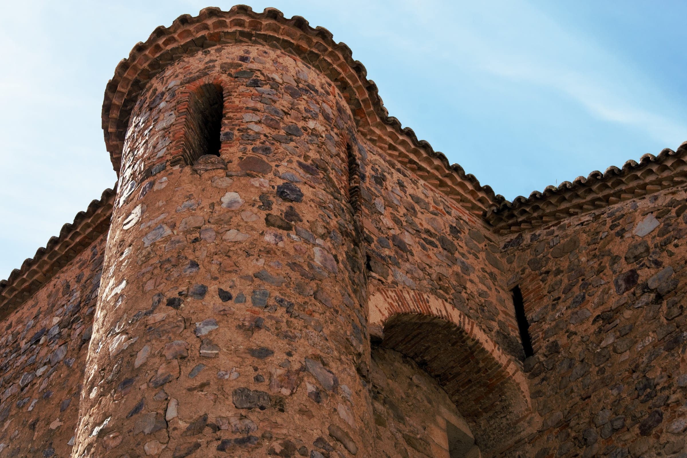 A round medieval tower and arched gateway of rubble stone and brick in Ciudad Real under a clear sky