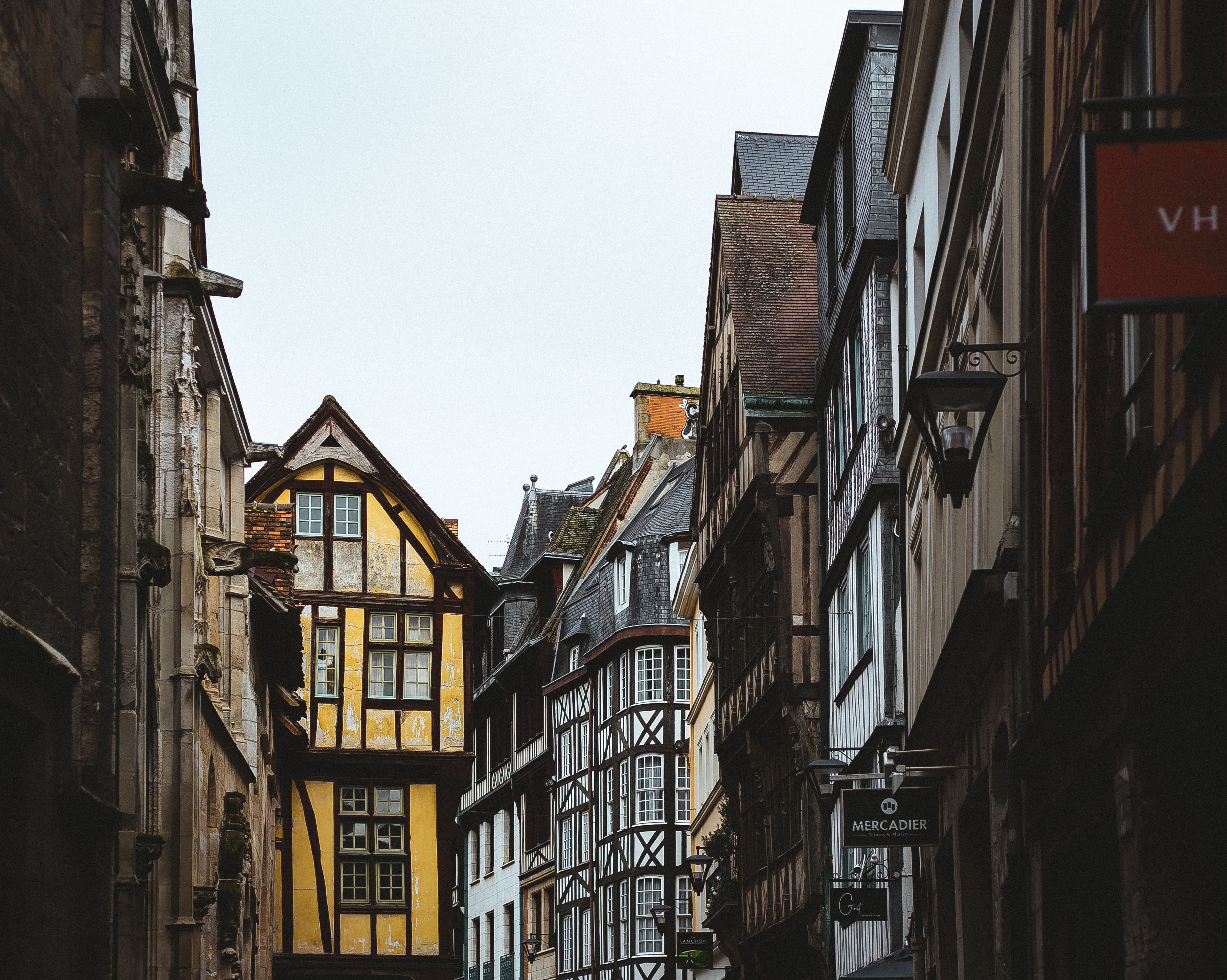 A narrow street of half-timbered houses in Rouen's old town, gargoyles and carved stone on the cathedral wall to the left, in the historic right-bank quarter the Seine-Marathon 76 course runs through at about km 2