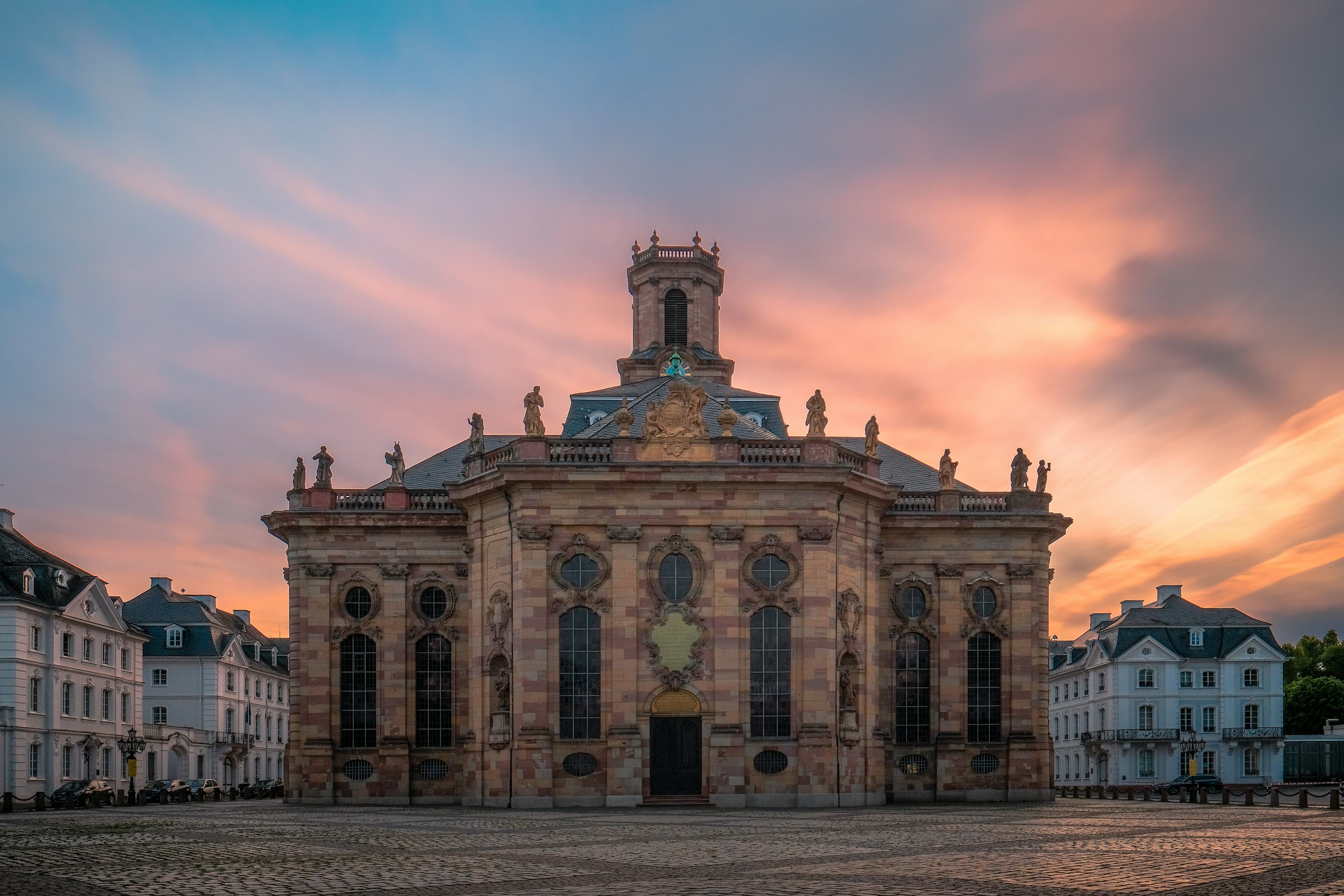The baroque Ludwigskirche and its cobbled square in Saarbrücken at sunset. The marathon runs along the Saar, not through this square, finishing about 3 km east at the Kulturbiergarten in St. Arnual.
