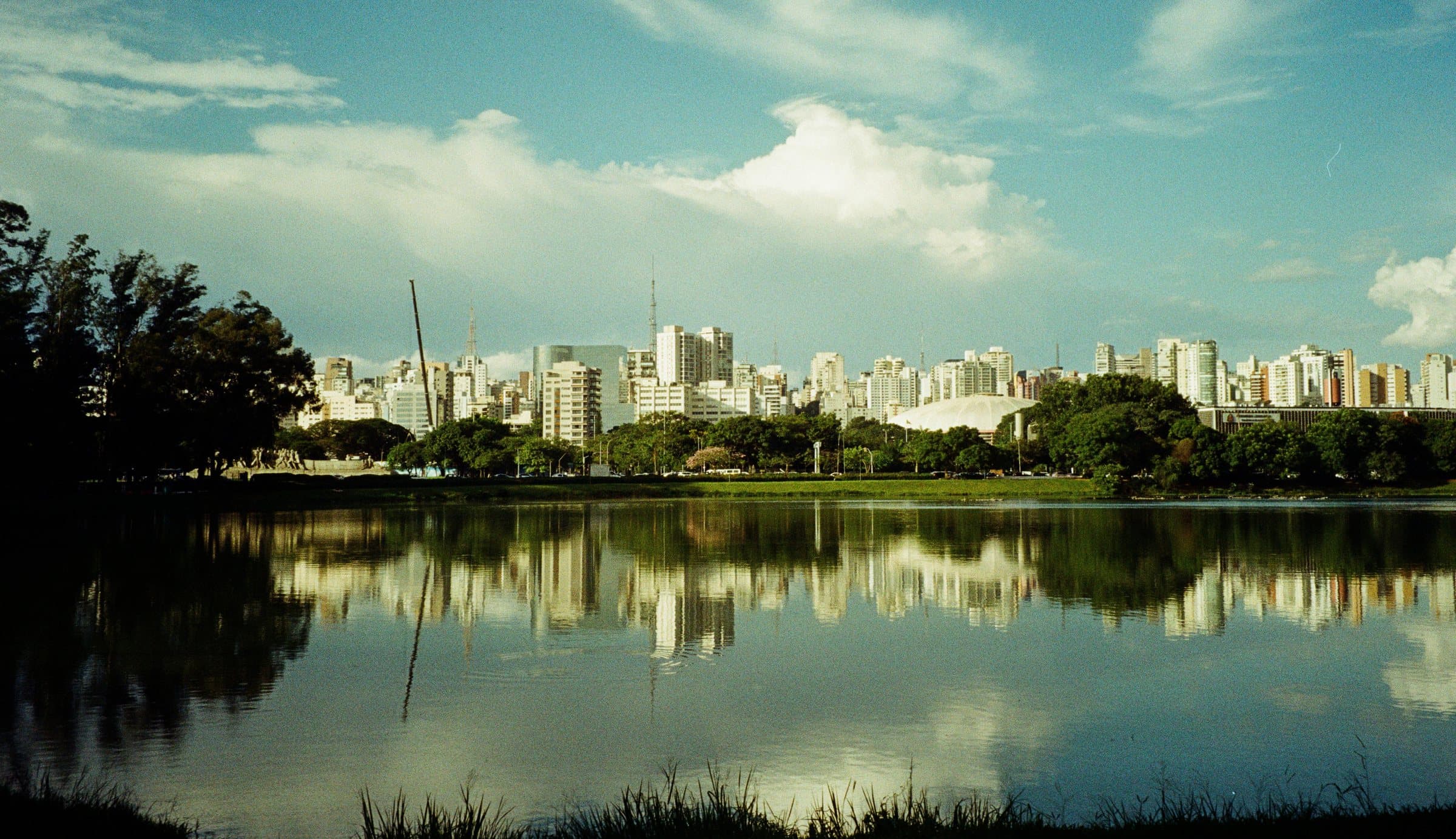 Apartment towers across the lake in Parque Ibirapuera, São Paulo, reflected in still water under scattered cloud