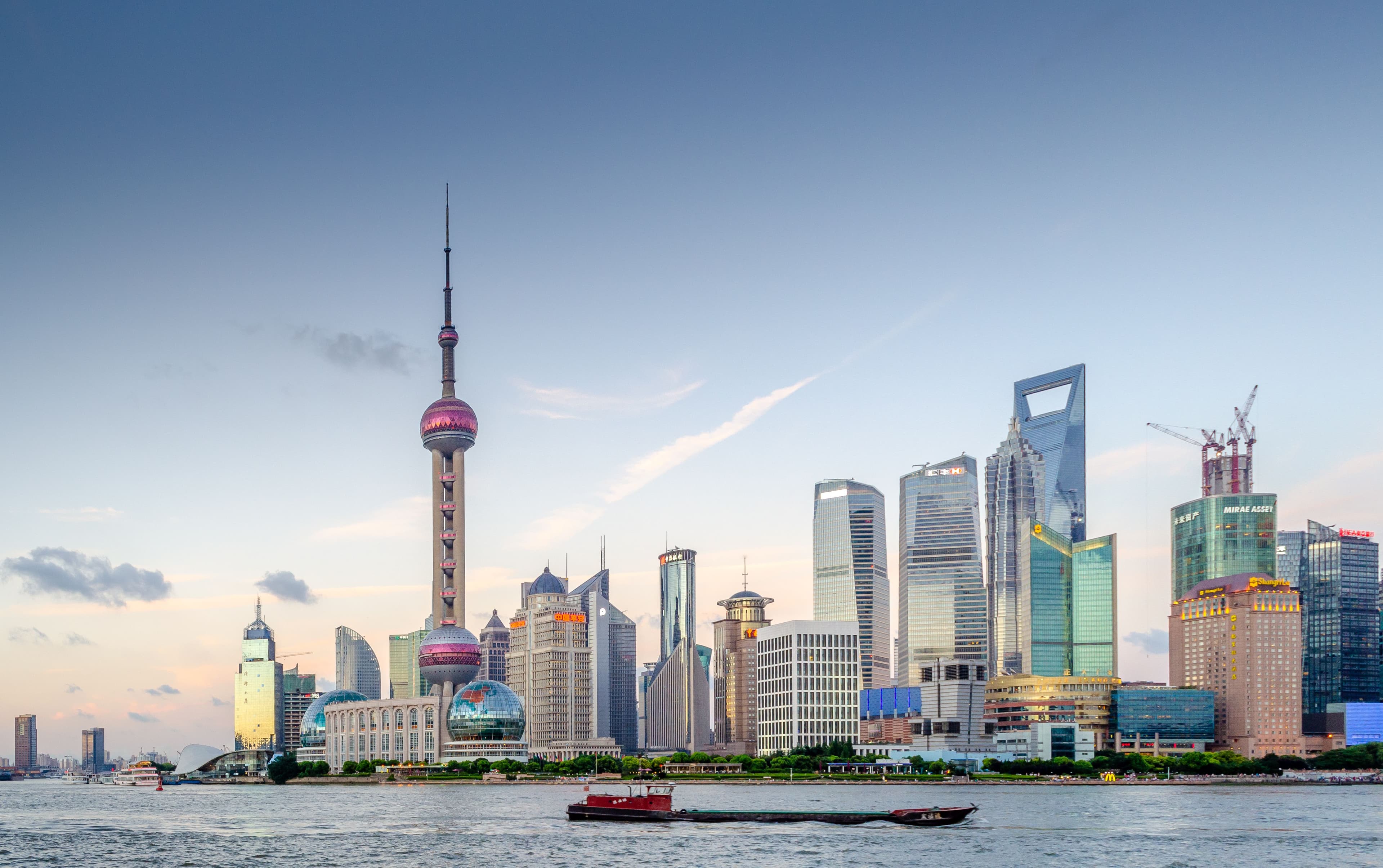 The Bund waterfront in Shanghai at dusk, with the Pudong skyline including the Oriental Pearl Tower visible across the Huangpu River