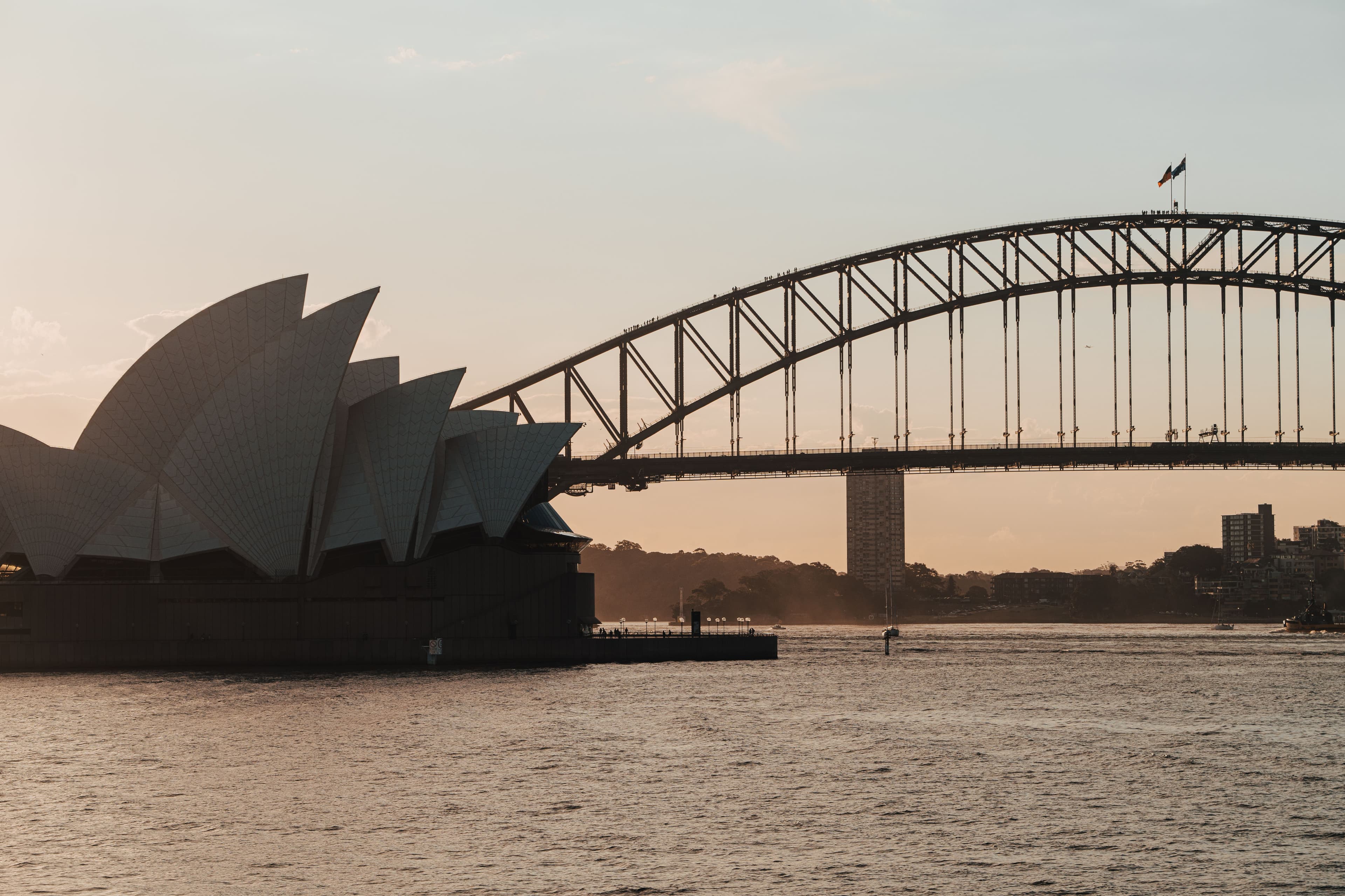 The Sydney Opera House sails and the Sydney Harbour Bridge in silhouette at sunset, seen from the east across the harbour, with North Sydney on the far shore. The TCS Sydney Marathon starts in North Sydney, crosses the bridge in the first 3 km and finishes on the Opera House Forecourt.
