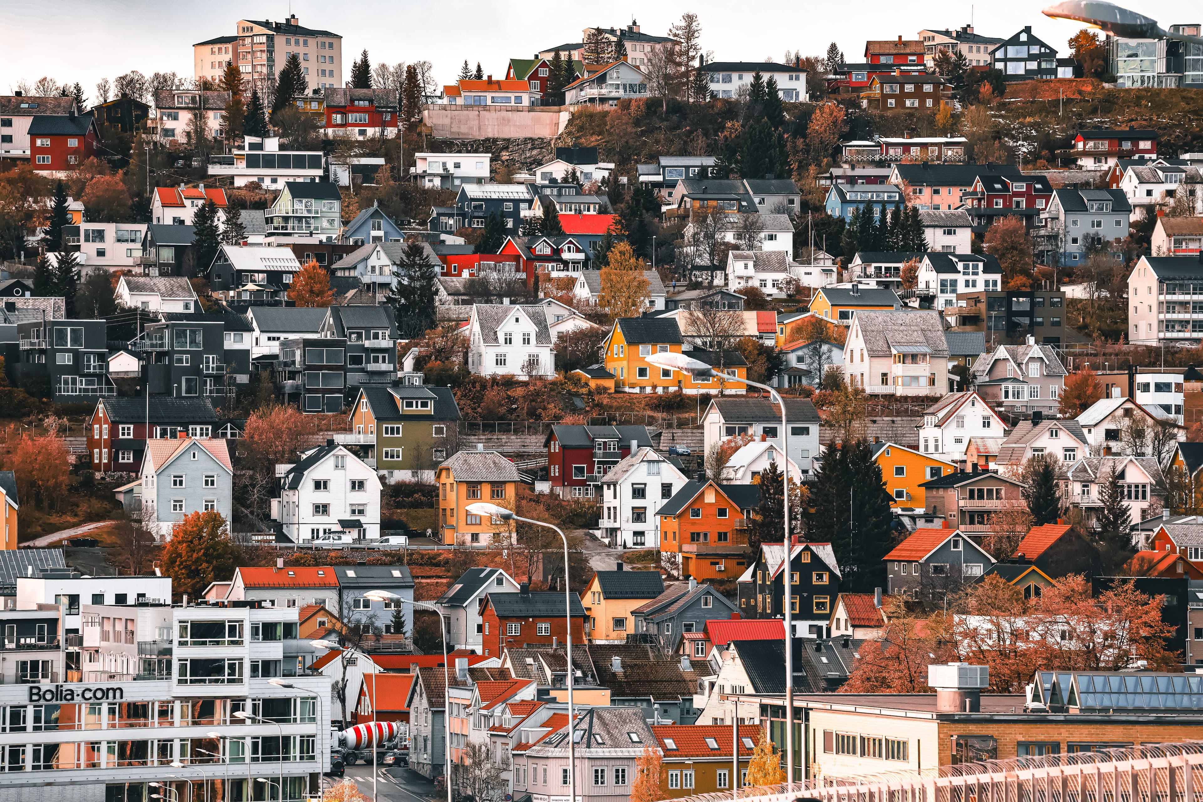 Colourful wooden houses clinging to the hillside on Tromsøya island, with the fjord and snow-dusted peaks of mainland Norway behind them