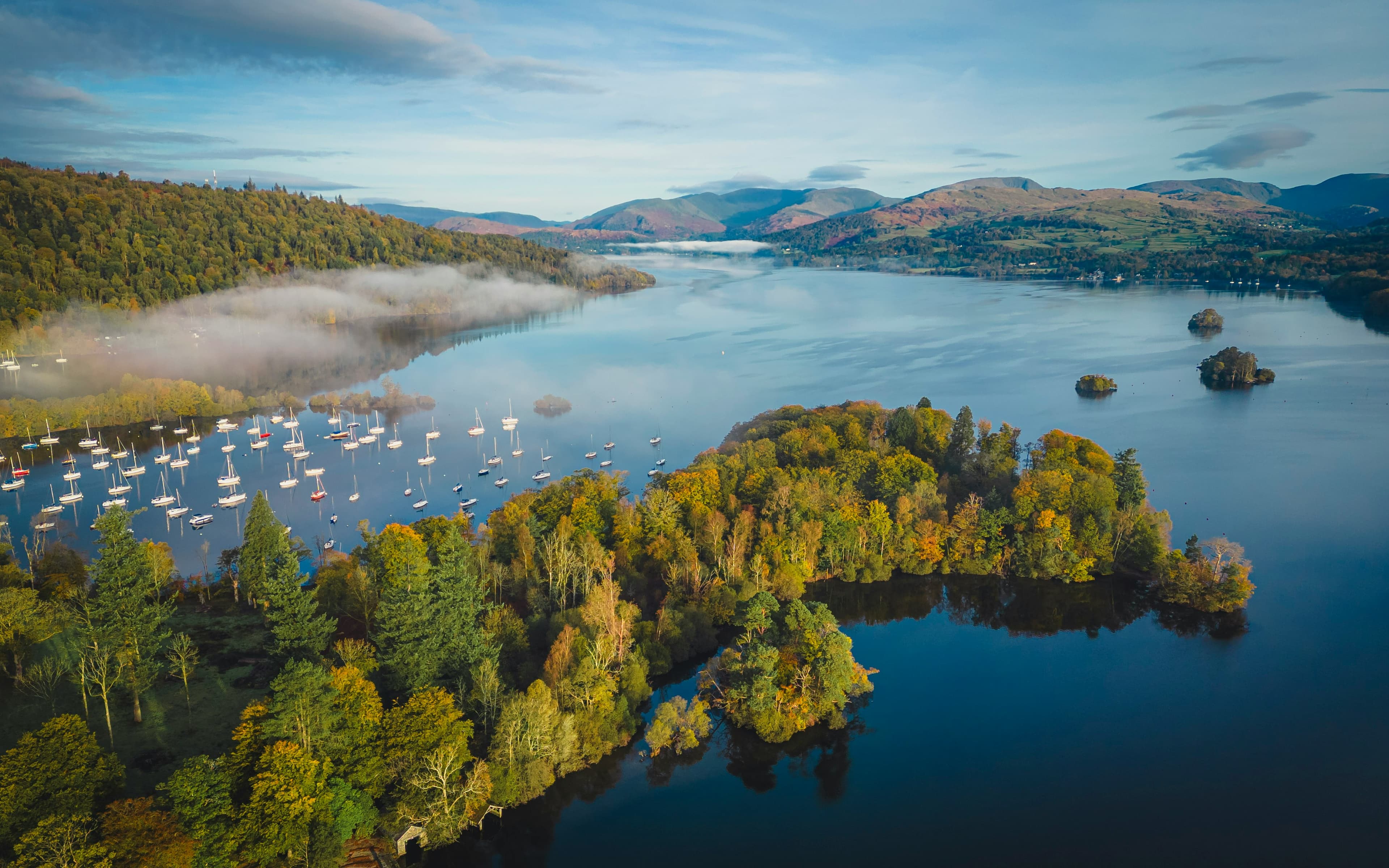 Aerial view of Windermere, England's largest lake, with moored sailing boats and wooded islands, near the Windermere Marathon's Ambleside start